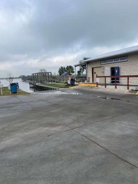 Wooden dock with open-air rectangular frames extending over calm water channel, boats on left, green foliage on sides.
