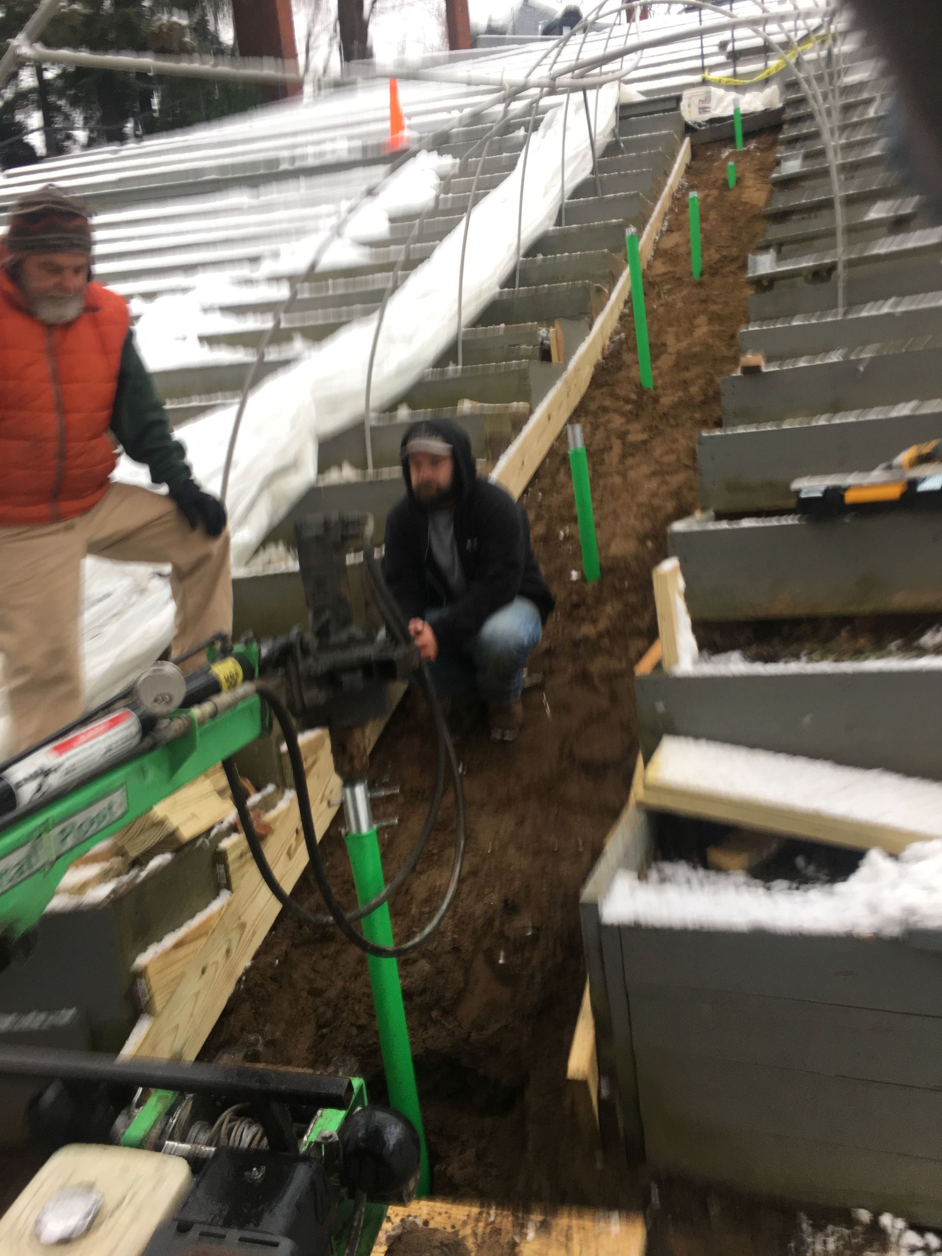 A man is kneeling in the dirt next to a green machine.