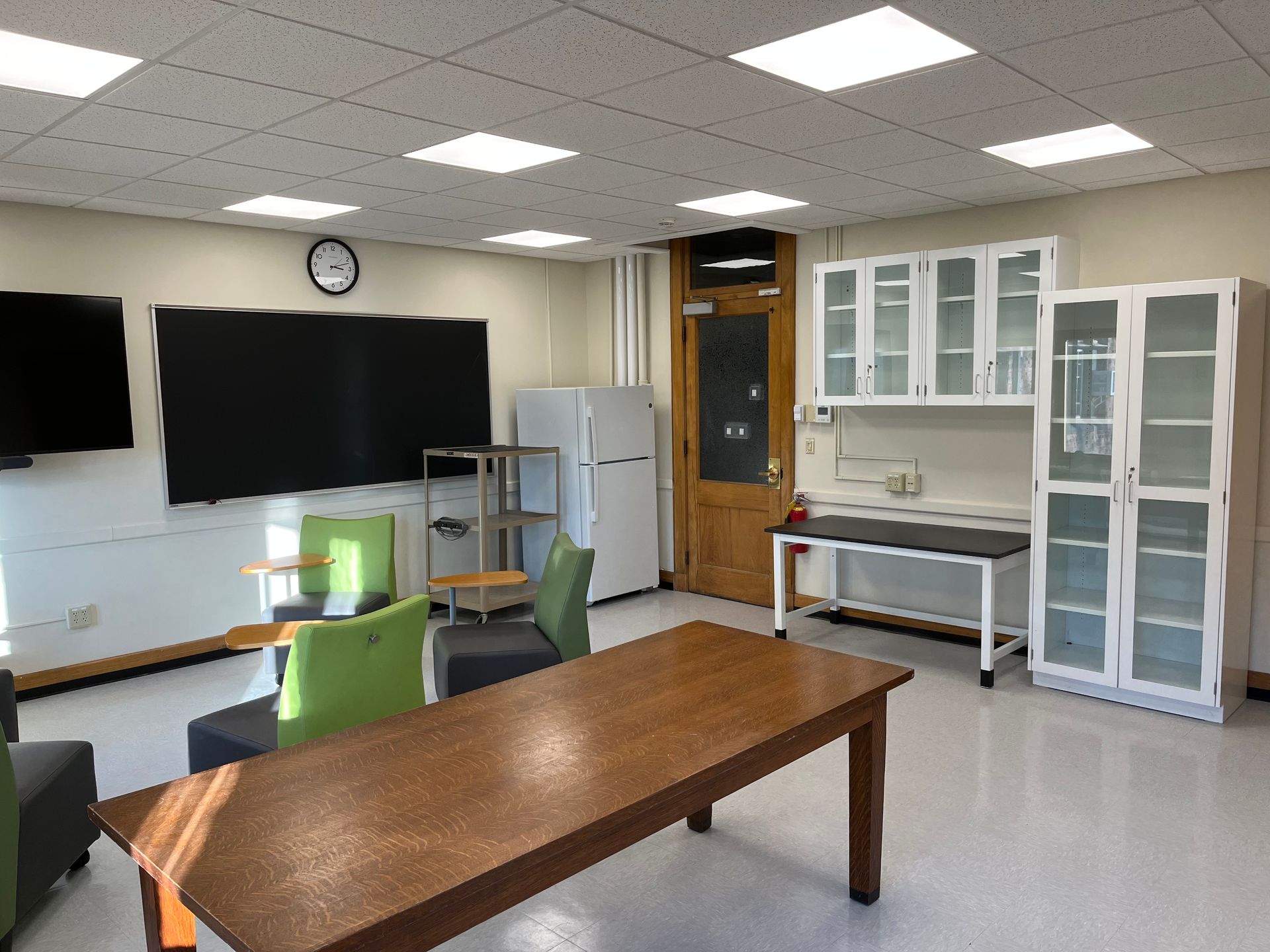 A large room with a table , chairs , cabinets and a refrigerator.