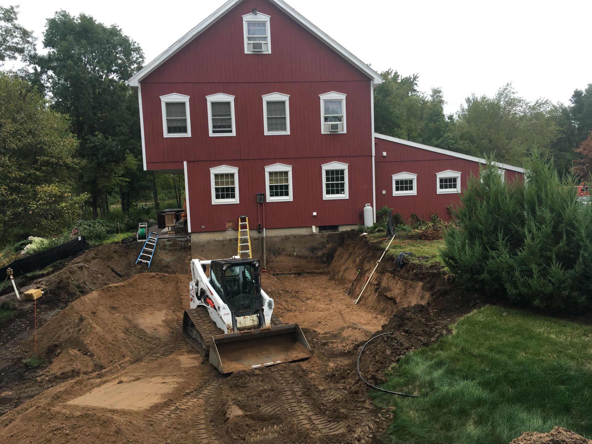 A bulldozer is digging a hole in front of a red barn.