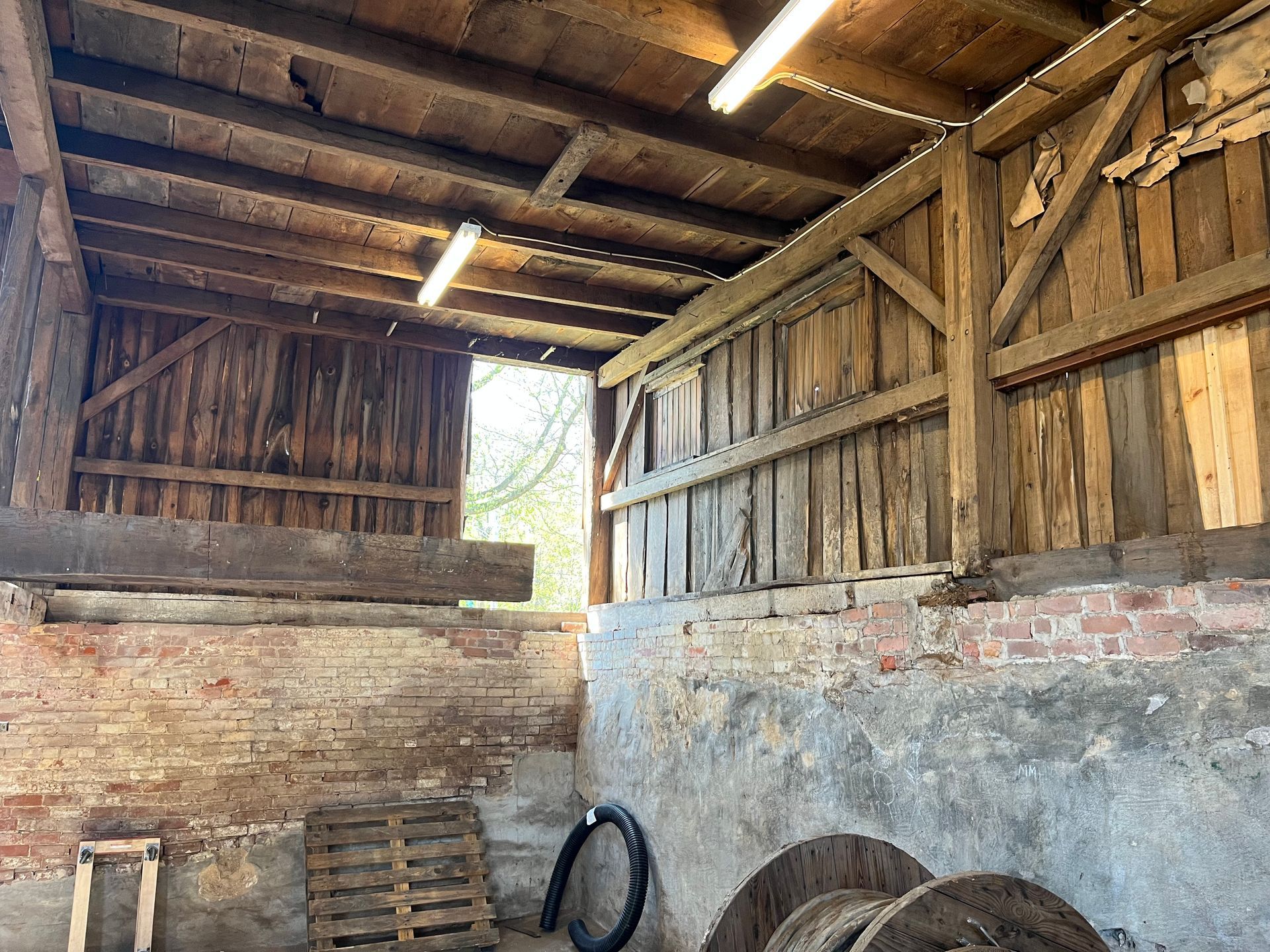 A wooden shed with a brick wall and a lot of wooden spools in it.