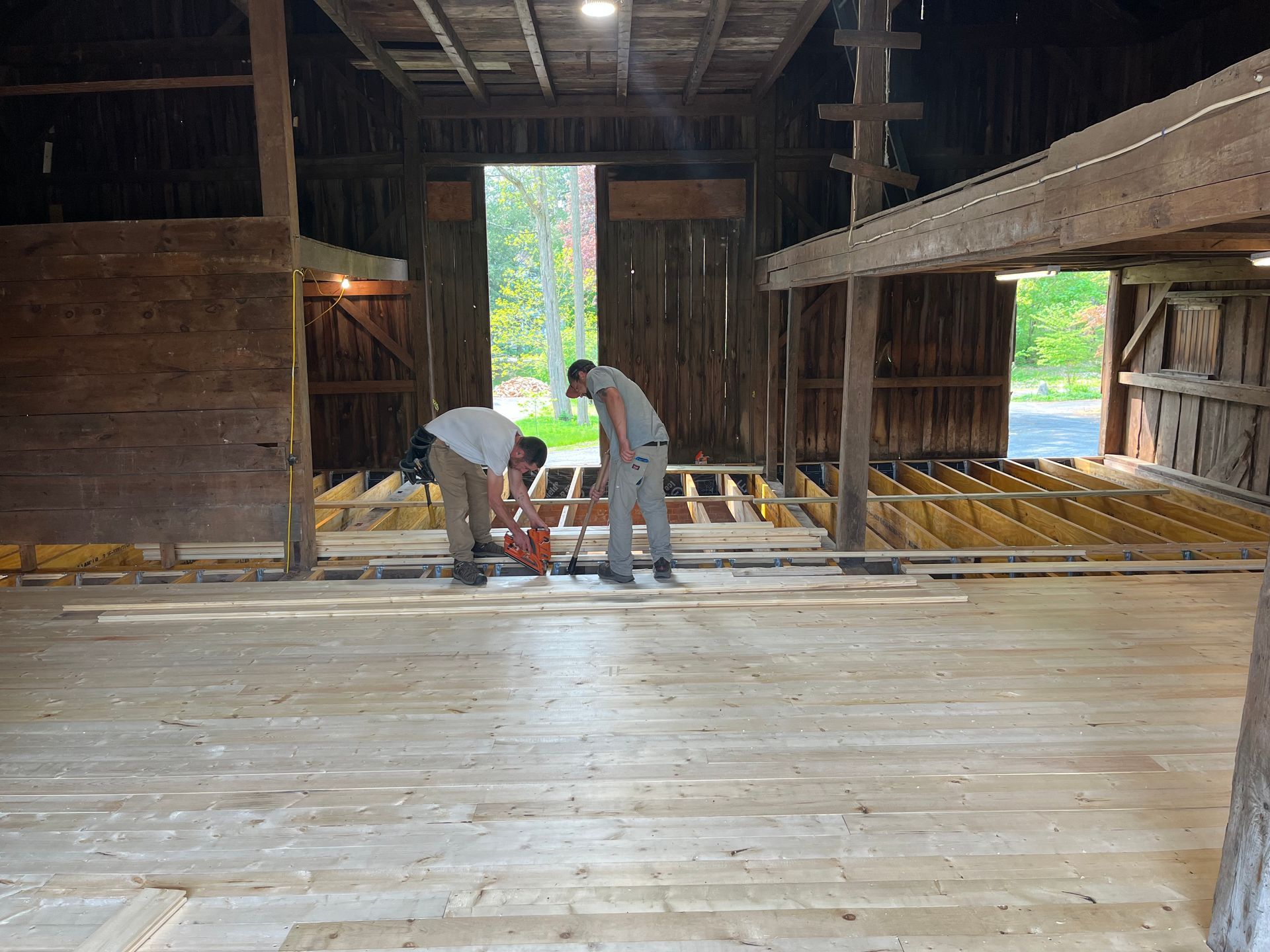 Two men are working on a wooden floor in a barn.