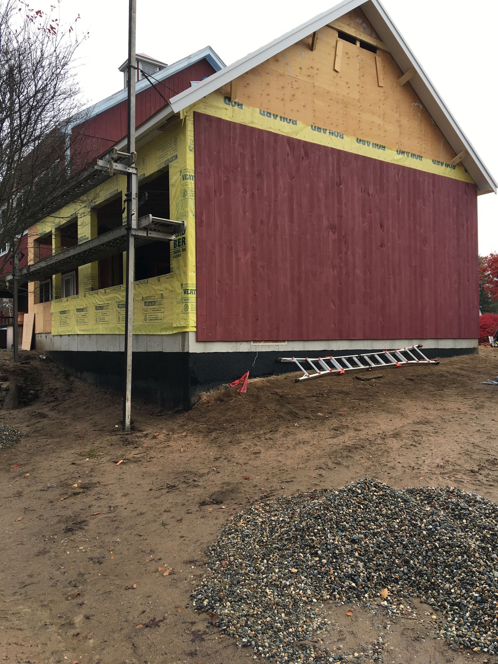 A red house is being built with a ladder in the dirt.