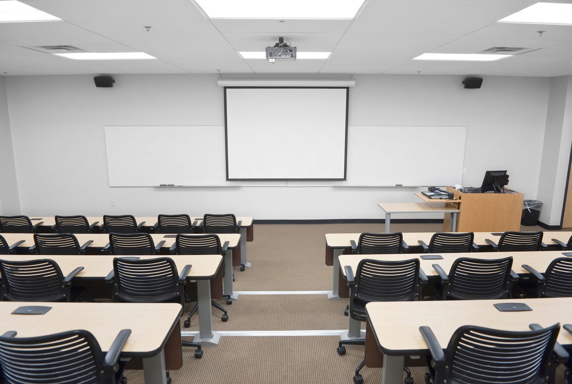 An empty classroom with tables and chairs and a projector screen.