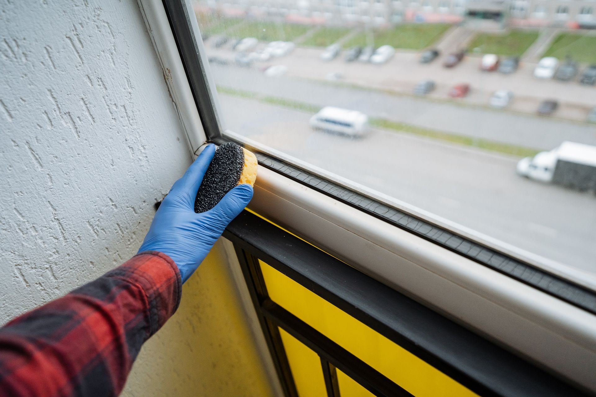 A gloved hand cleaning a windowsill with a view of passing traffic.