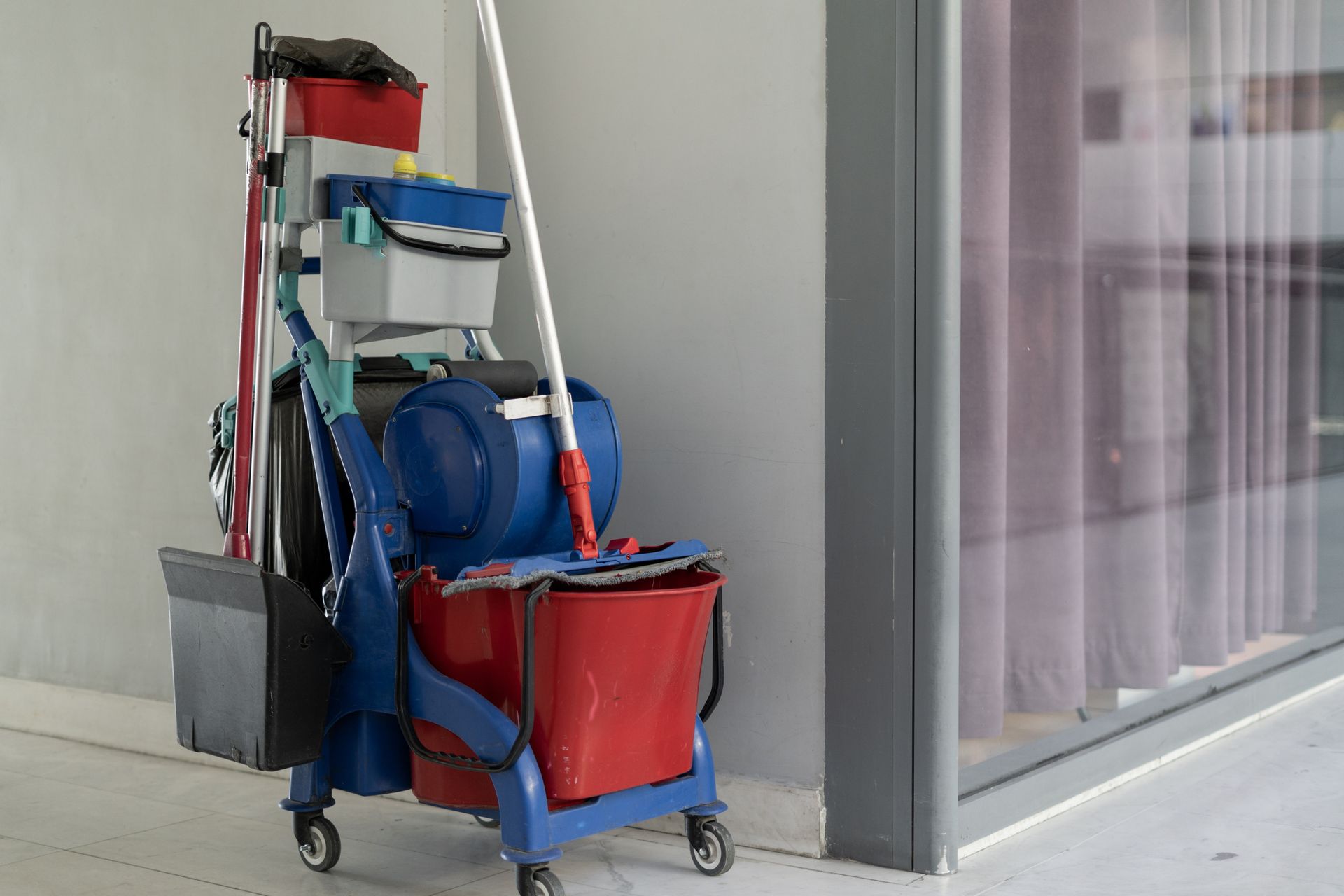 A trolley with cleaning tools is parked in a hallway besides an office space.