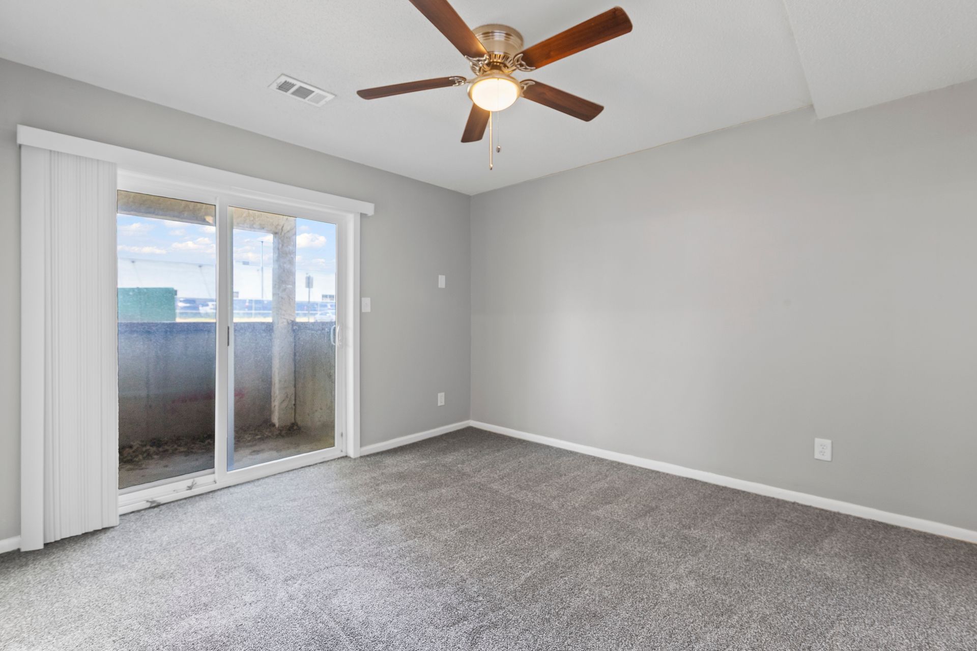 Empty bedroom with gray carpet, sliding glass door to balcony, ceiling fan.