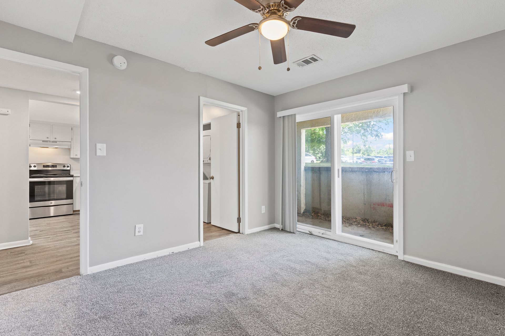 Bedroom with gray walls, carpet, ceiling fan, sliding glass door to a balcony, and doorways to the kitchen and hallway.