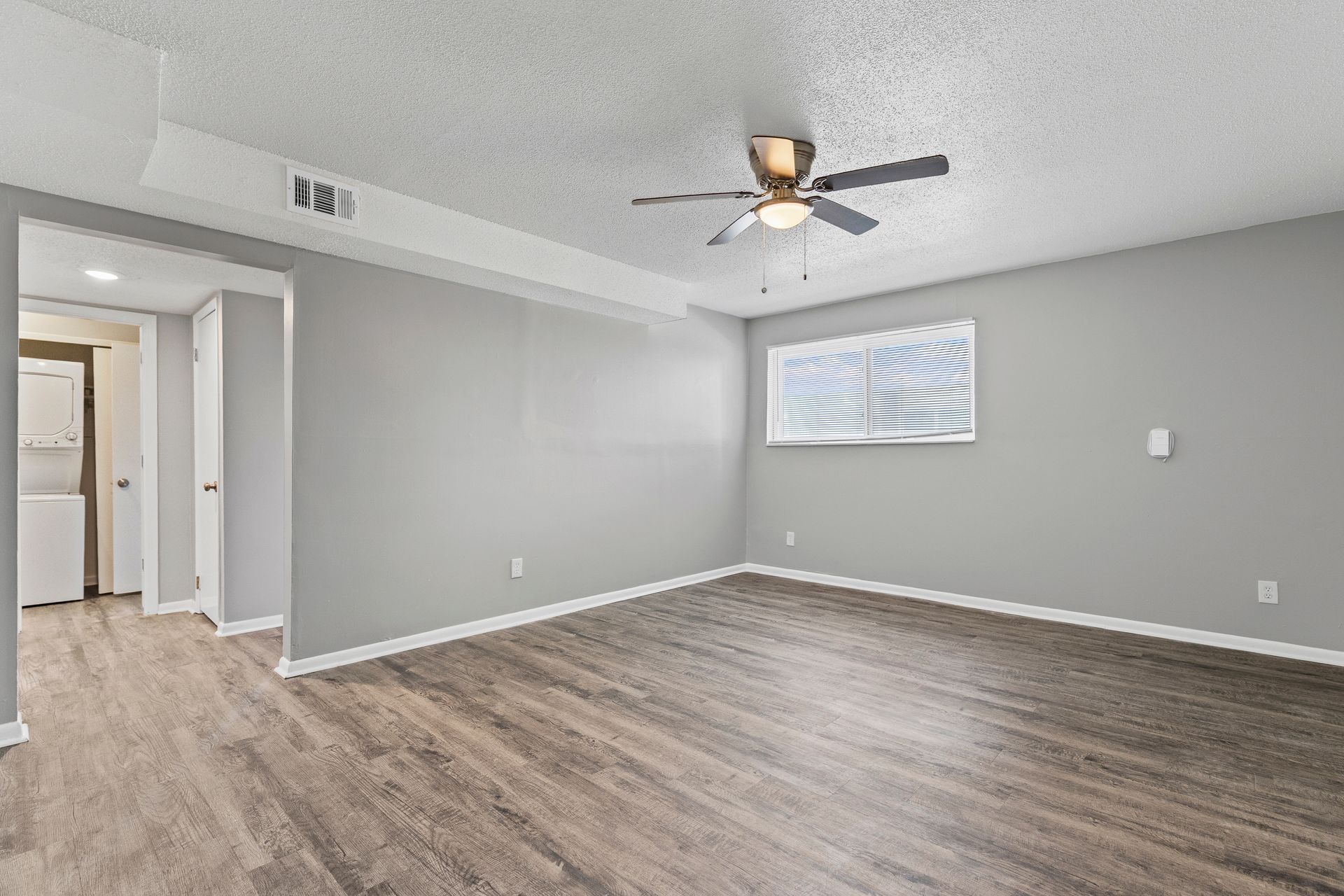 Empty room with gray walls, wood floors, and a ceiling fan.