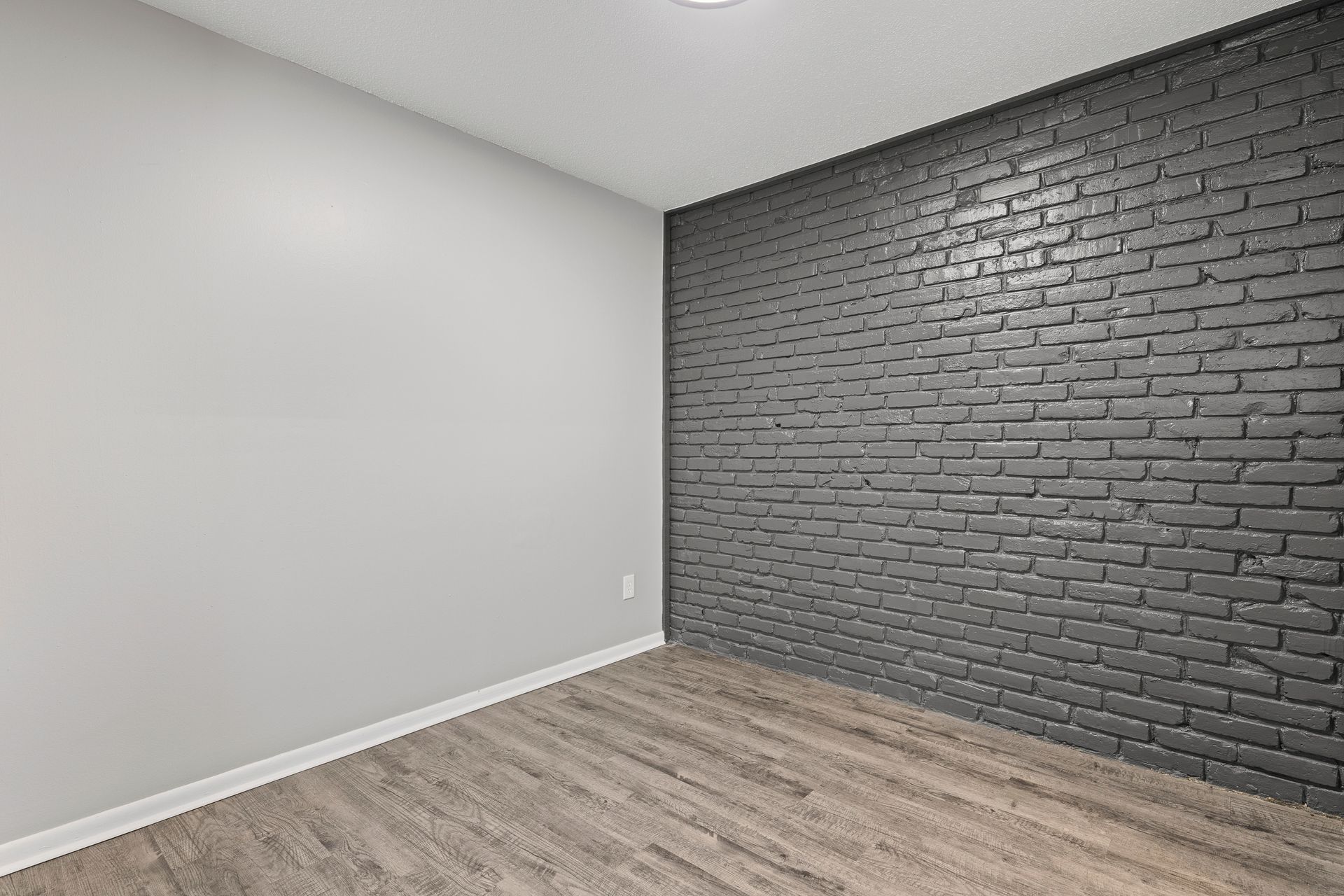 Empty room with wood floor, white and dark gray brick walls.