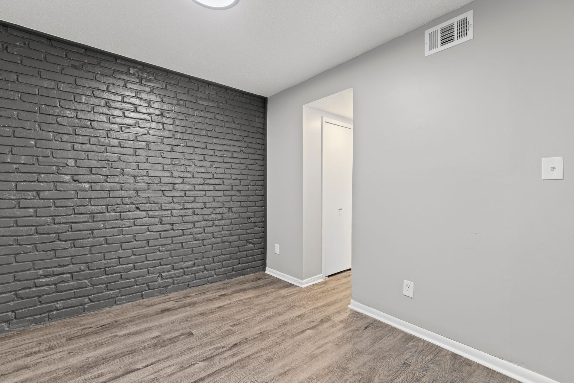 Interior view of a room with gray brick wall, gray walls, wooden floor, and a doorway.