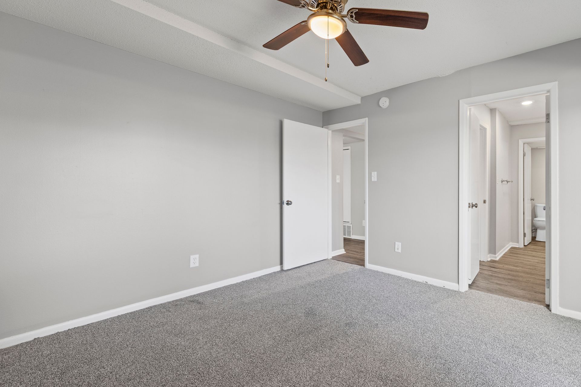 Bedroom with gray walls, carpet, ceiling fan, and open doorways.