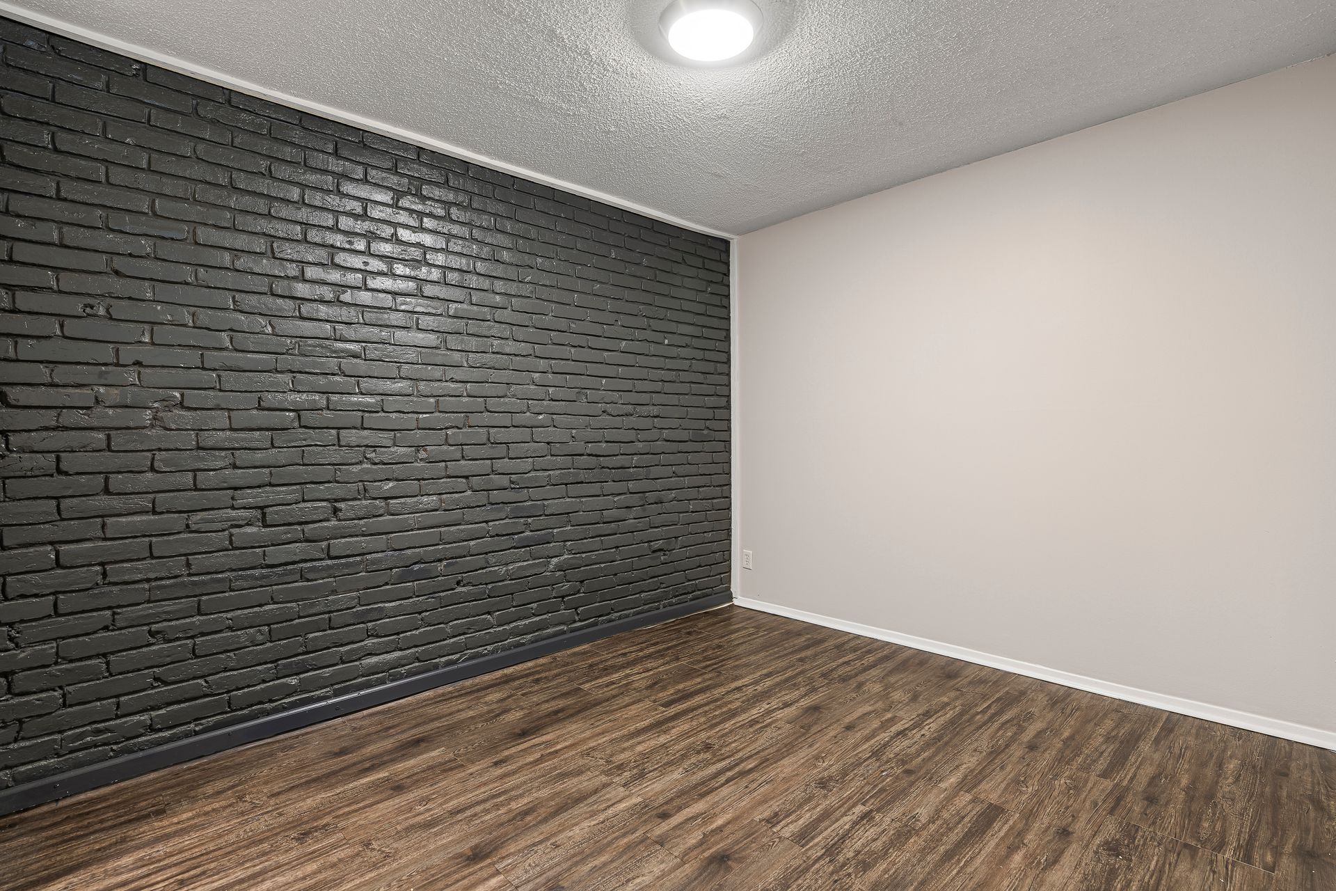 Empty room with black brick wall, white wall, wood floor, and ceiling light.