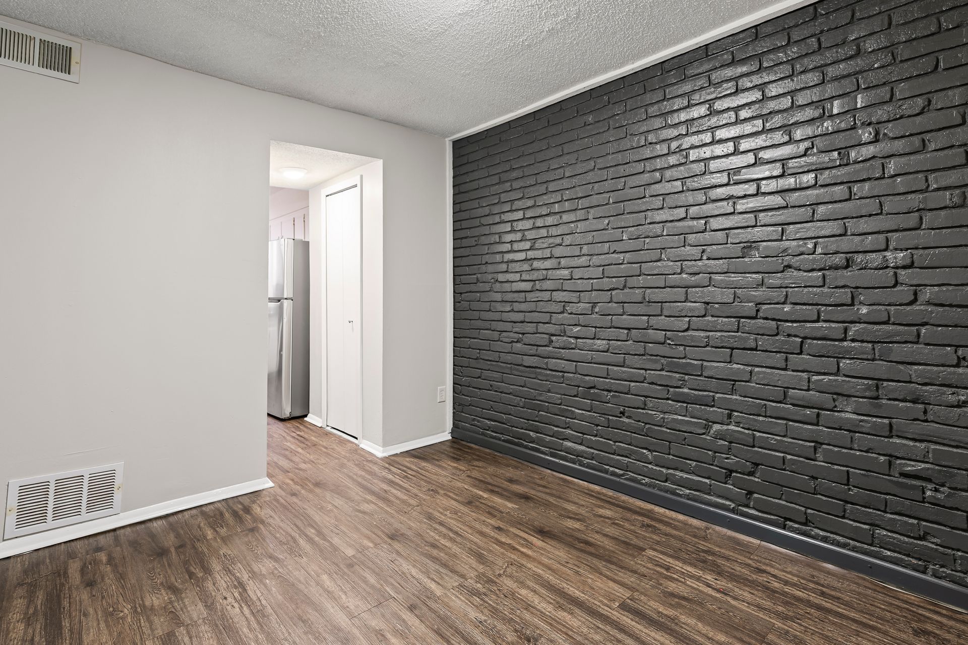 Empty room with dark gray brick accent wall, gray painted walls, and wood-look flooring.