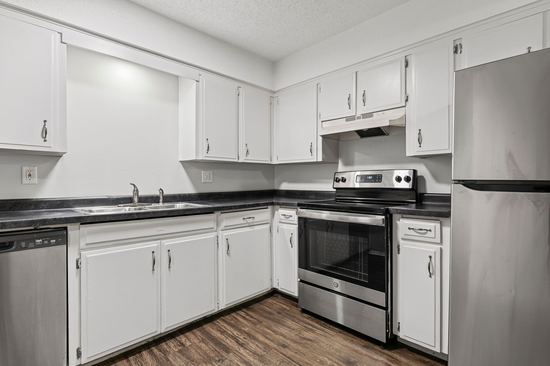 White kitchen with stainless steel appliances and dark countertops.