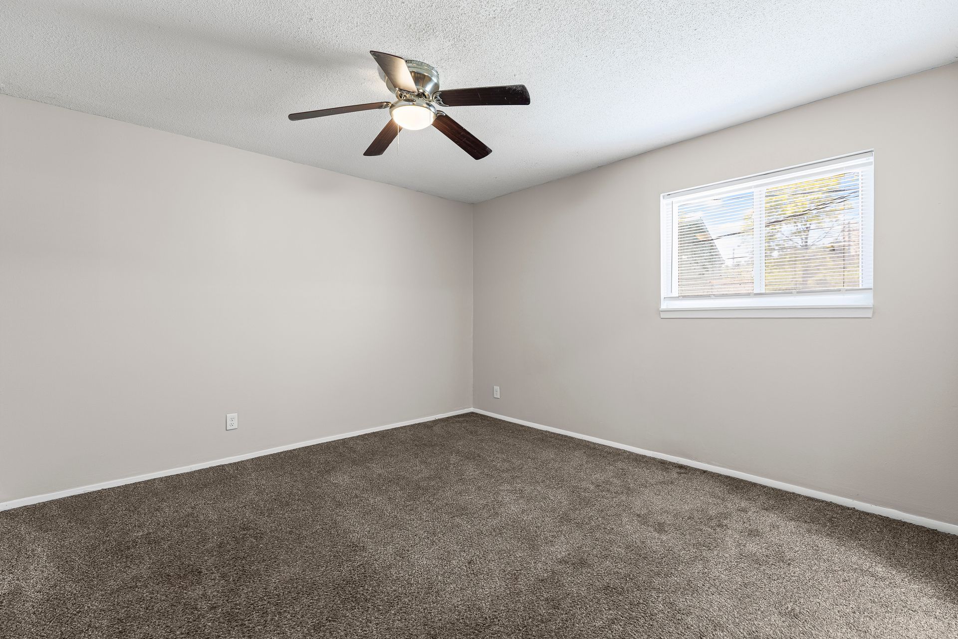 Empty room with brown carpet, tan walls, ceiling fan, and small window.