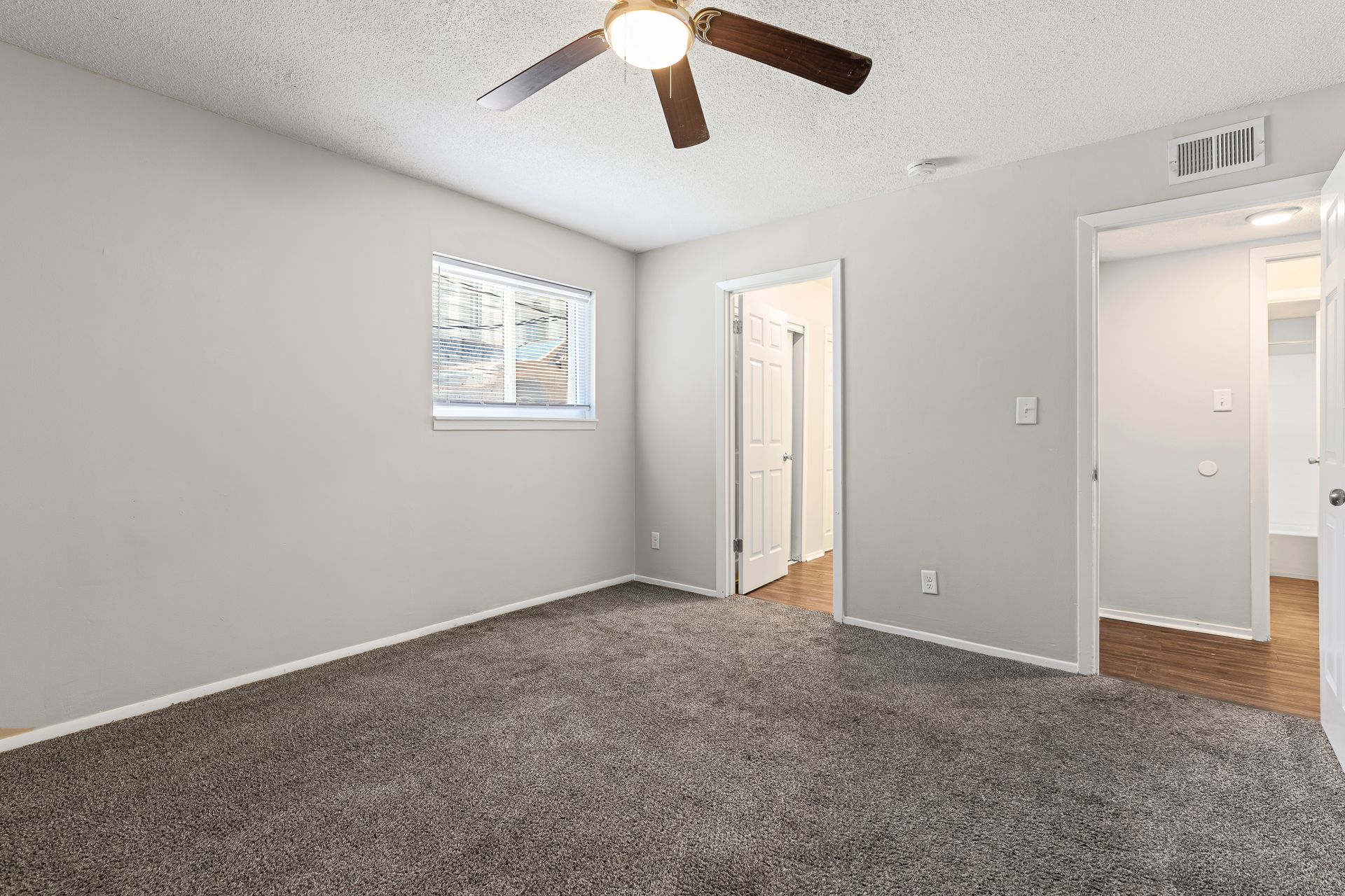Bedroom with gray walls and carpet, window, white door, and ceiling fan.