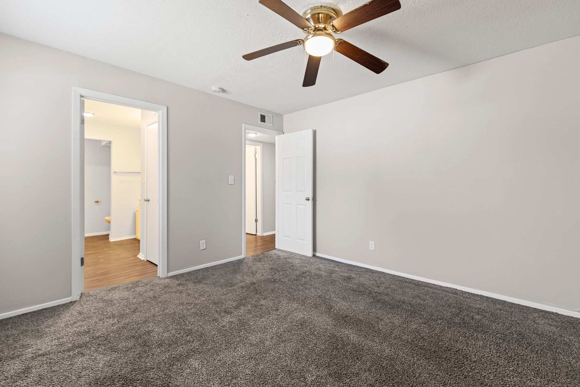 Bedroom with gray carpet, ceiling fan, and doorways to other rooms.
