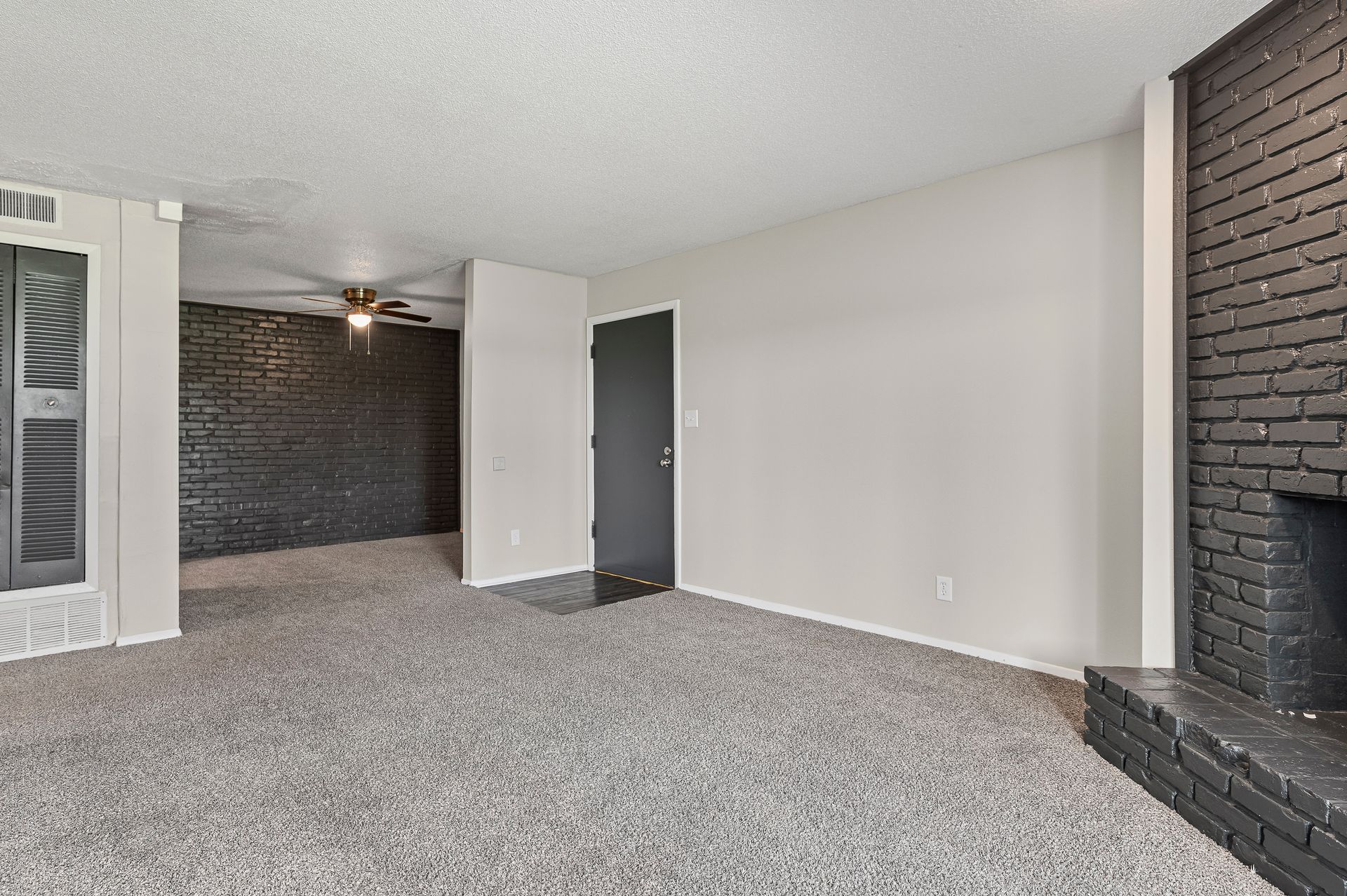 Empty living room with gray carpet, black fireplace, and black accent wall.
