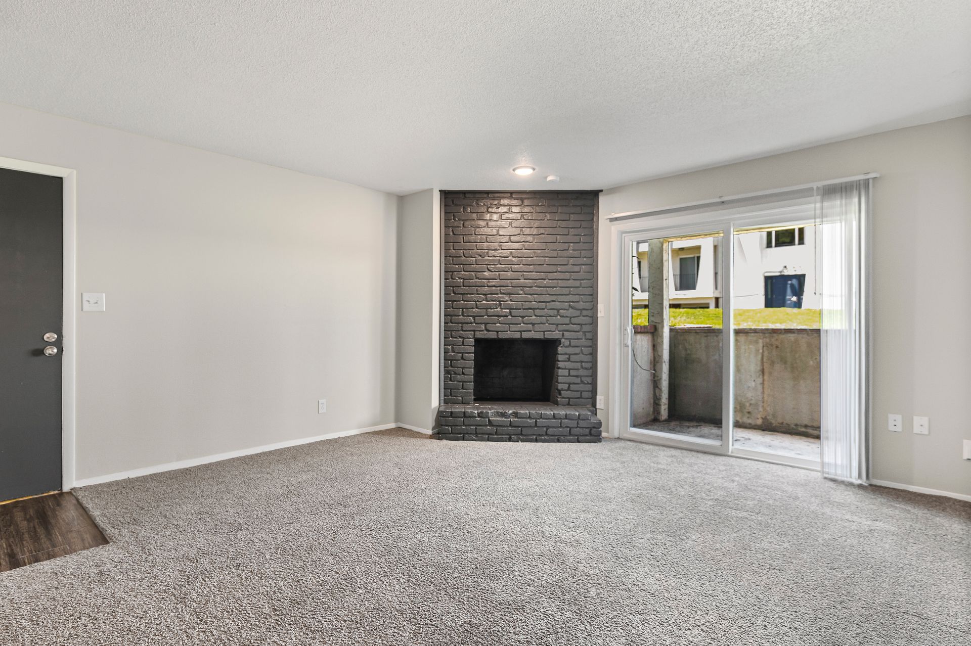 Living room with grey walls, carpet, brick fireplace, and sliding glass door to a patio.
