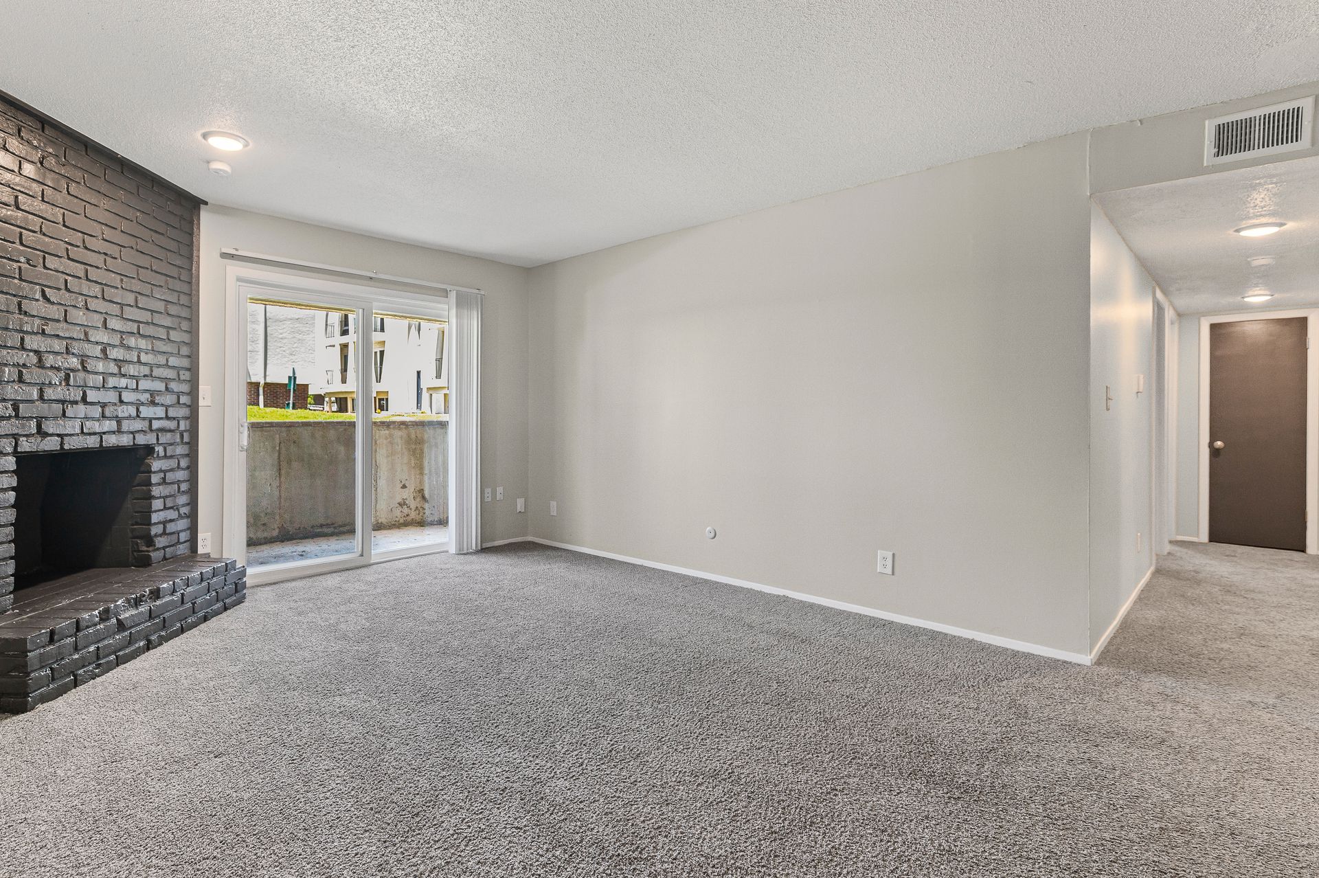 Empty living room with gray carpet, a fireplace, and sliding glass doors.