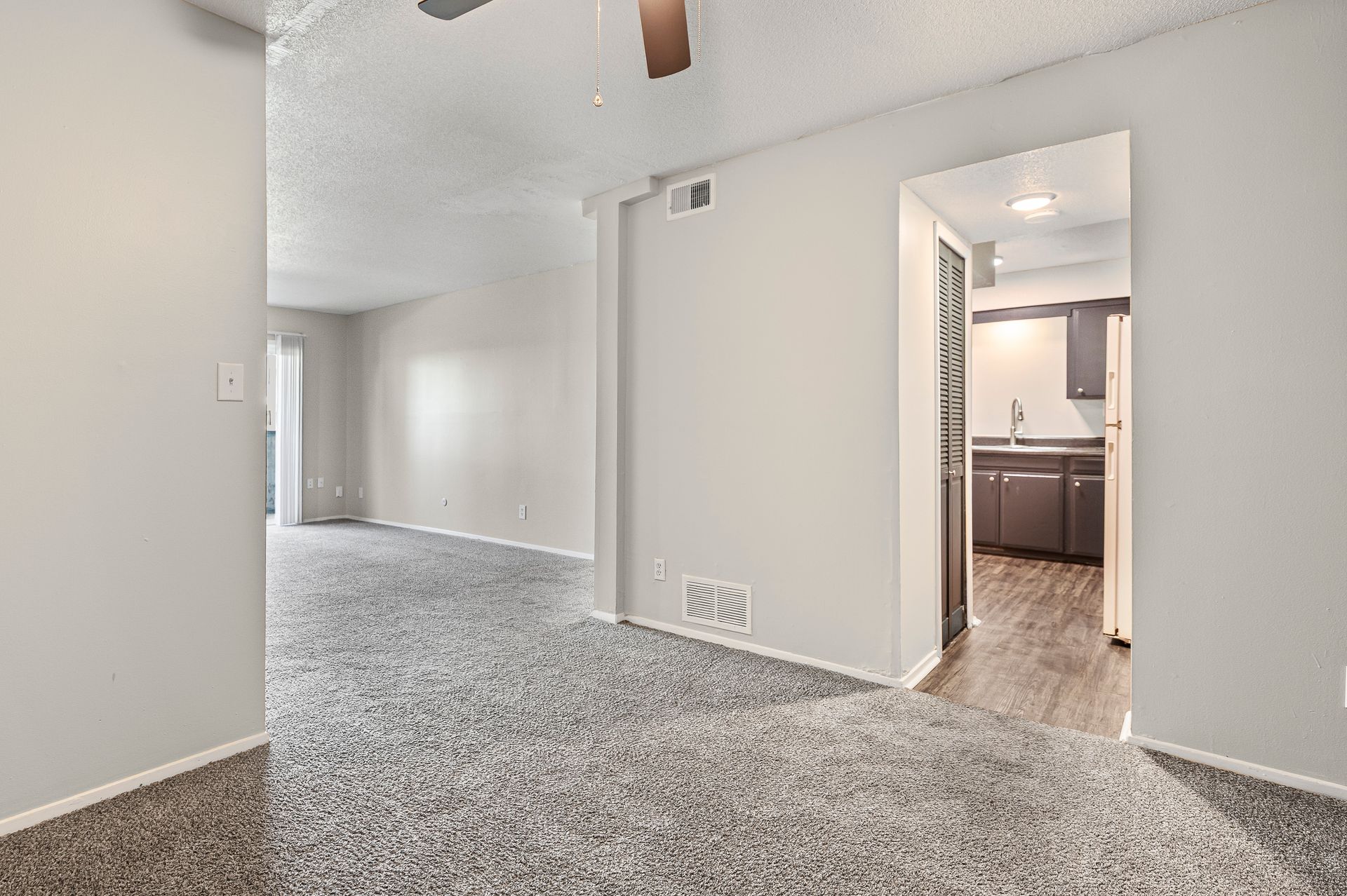 Empty apartment living room, neutral colors, carpet, doorway to kitchen, and another room.