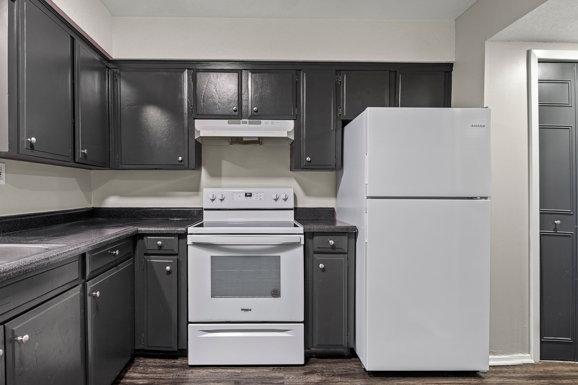 Dark-painted kitchen with white stove, refrigerator, and cabinets.