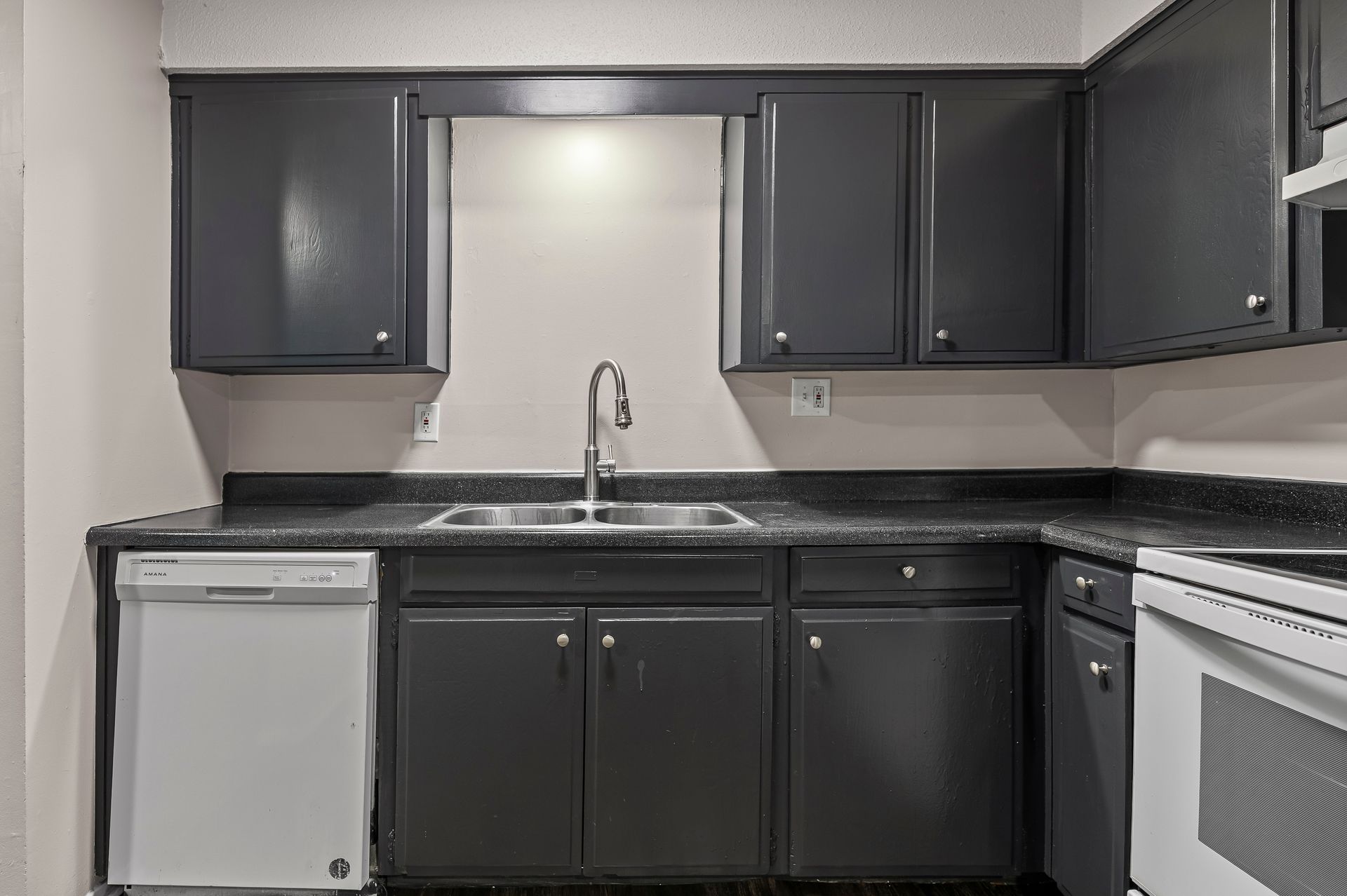 Dark gray kitchen cabinets and countertops, white appliances. Sink area.