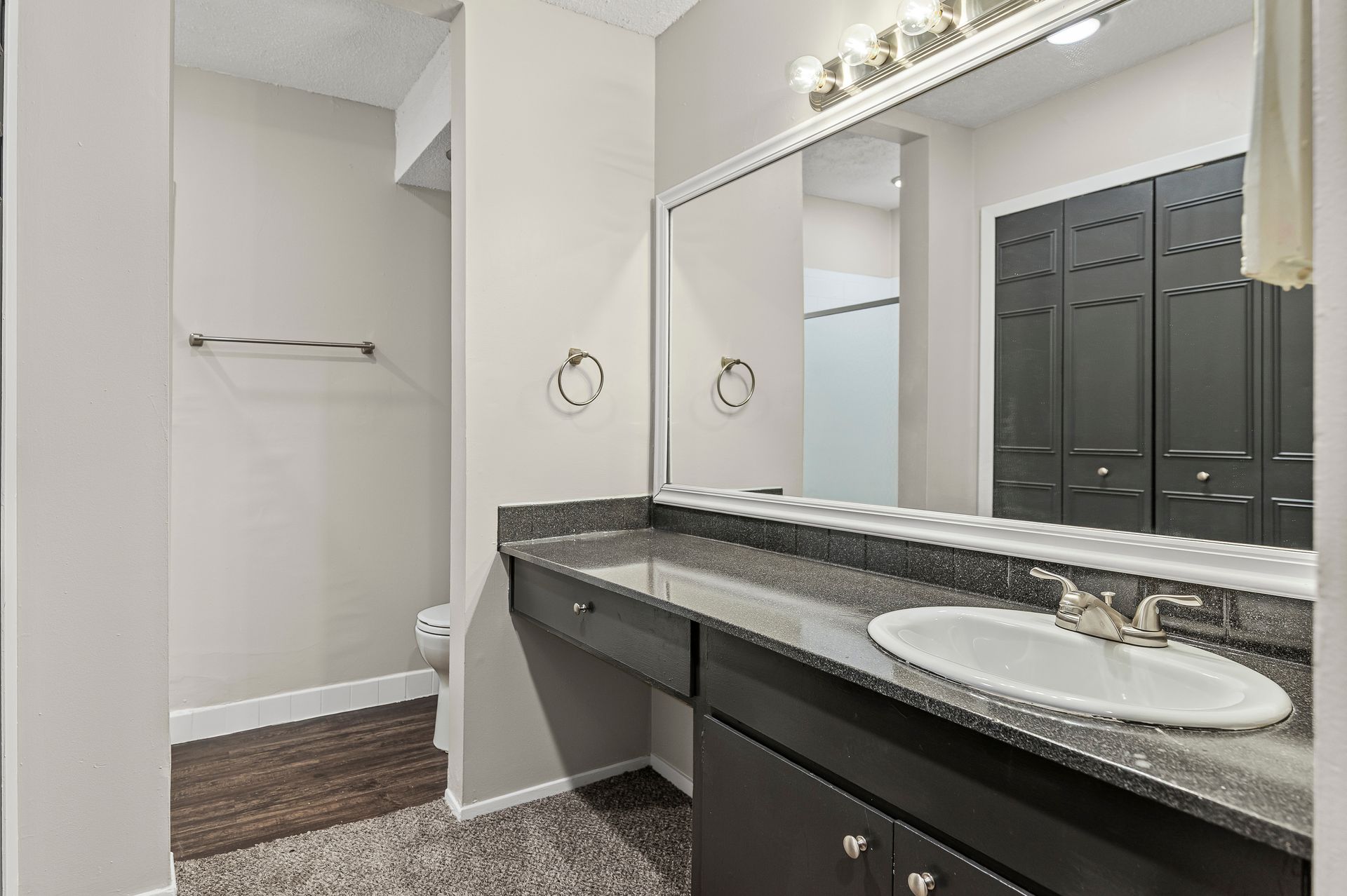 Bathroom with dark cabinets, granite countertop, large mirror, and dark closet doors.
