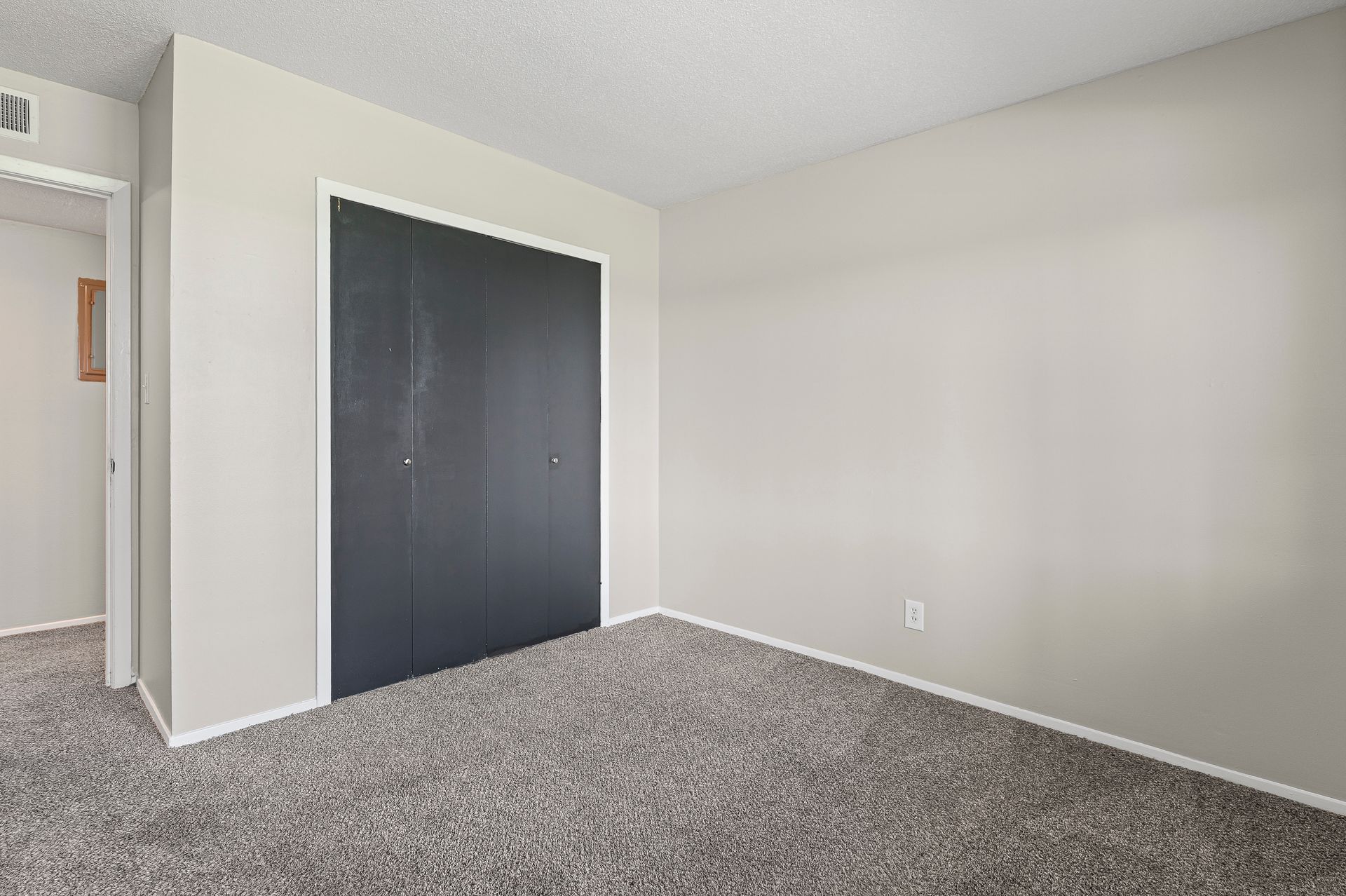 Empty bedroom with gray carpet, black closet doors, and light gray walls.
