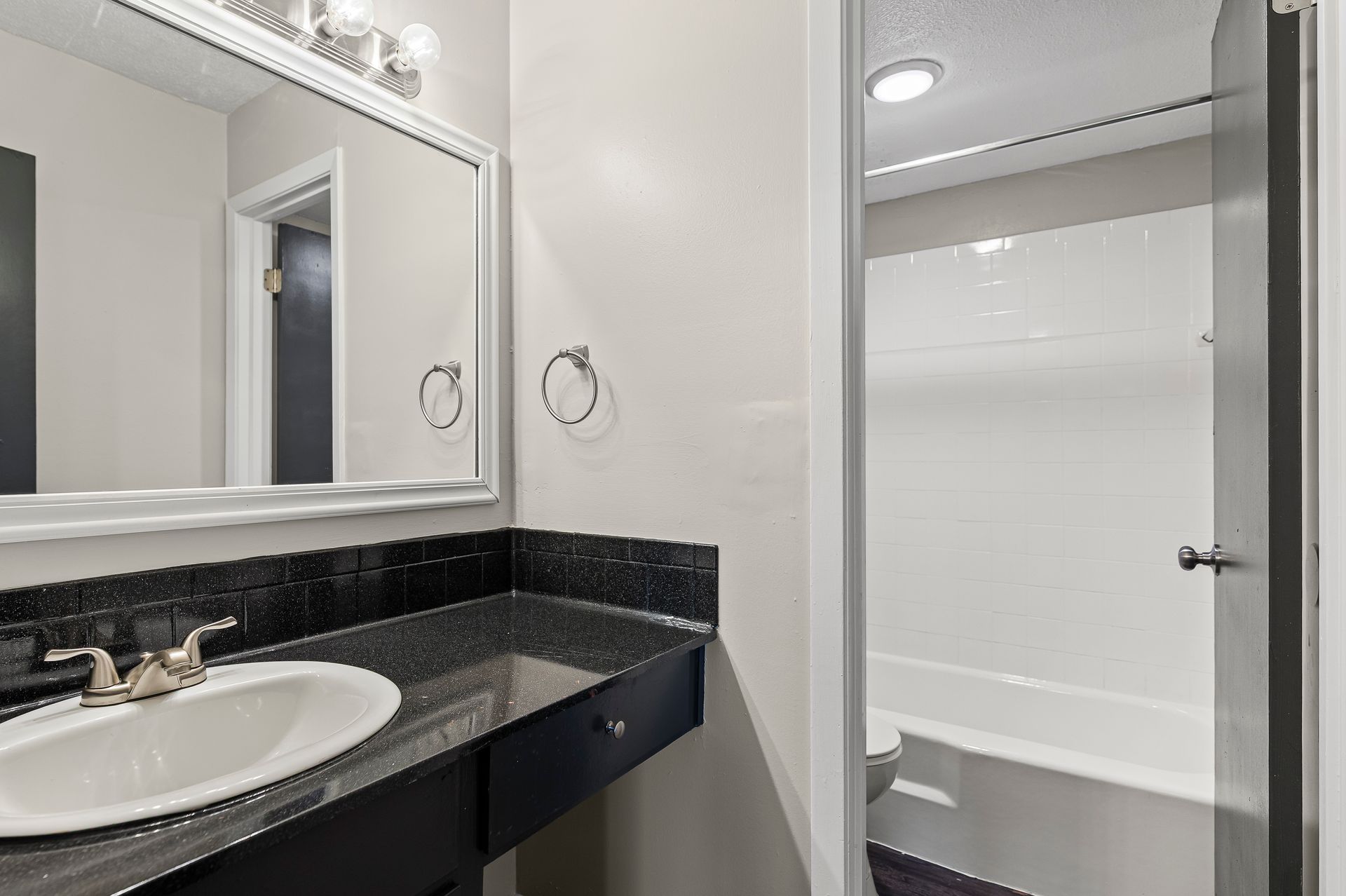 Bathroom with a black granite countertop, white sink, large mirror, and a doorway to the bathtub and toilet.