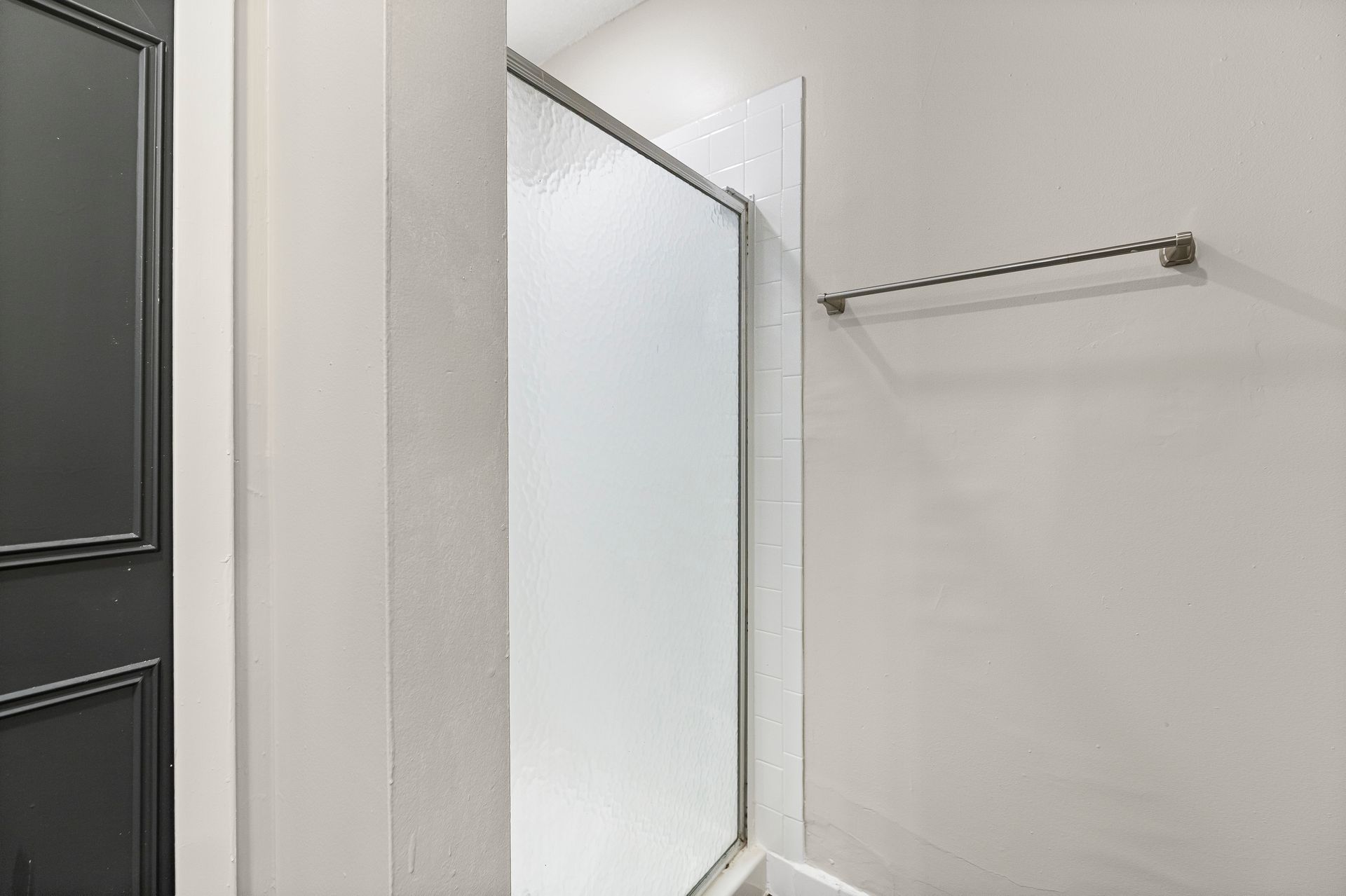 Frosted glass shower door in a bathroom with a towel rack and gray door.