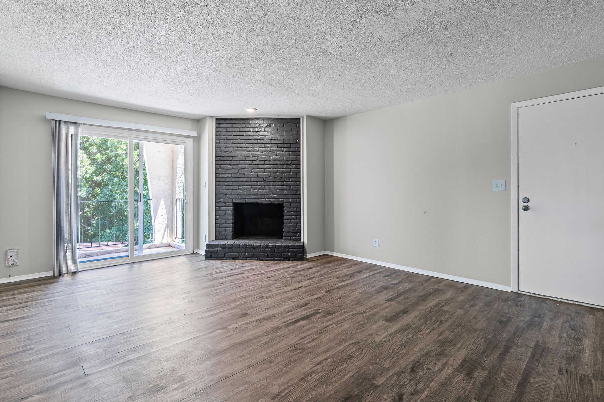 Empty living room with fireplace, sliding glass door, and wood-look floors.