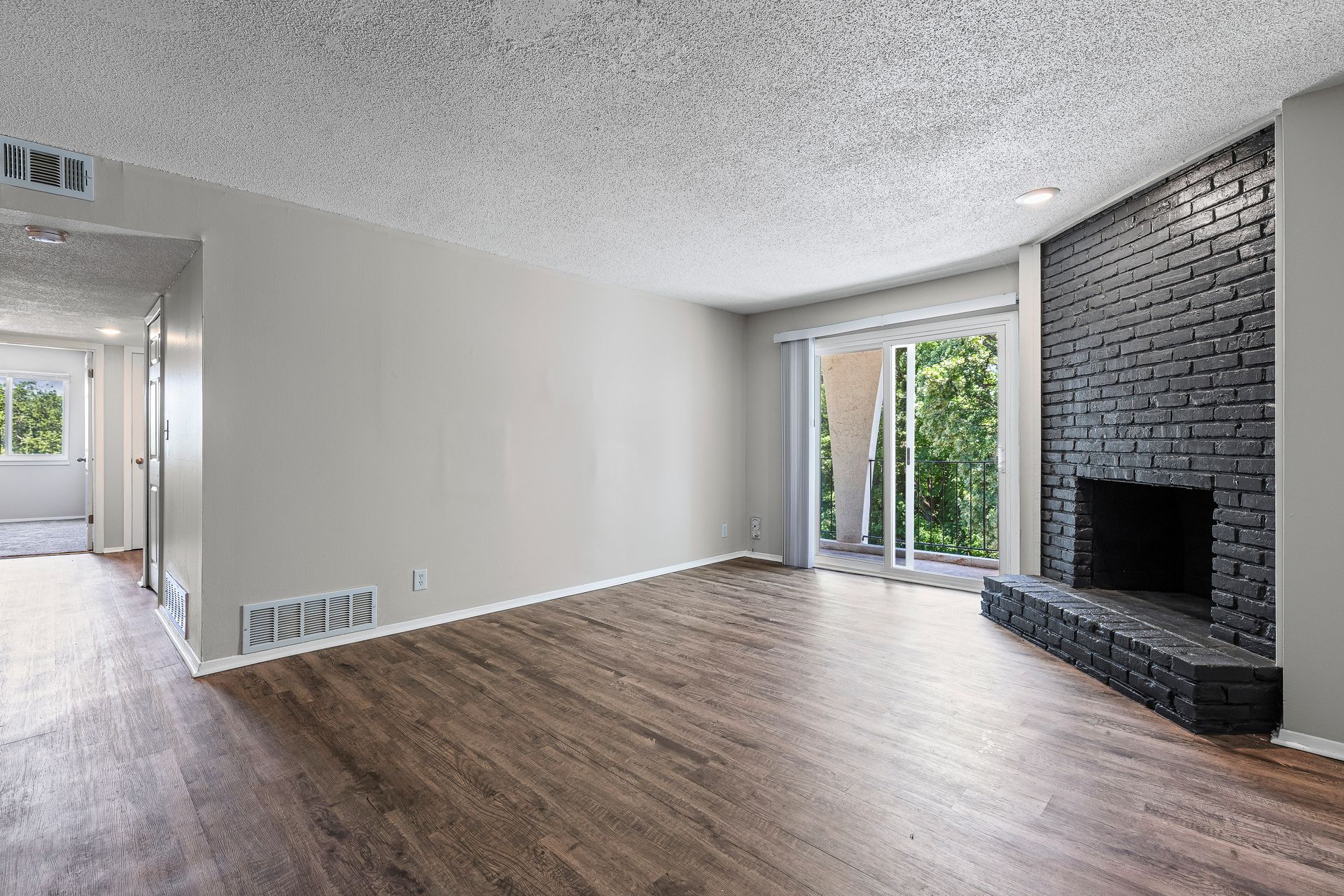 Empty living room with hardwood floors, a gray brick fireplace, and a sliding glass door to a balcony.