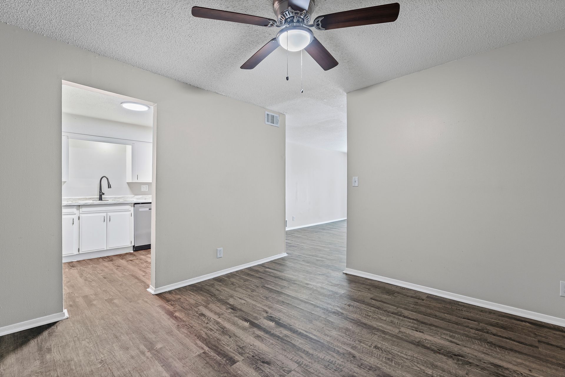 Living room with gray walls, wood-look floor, doorway to kitchen, ceiling fan.