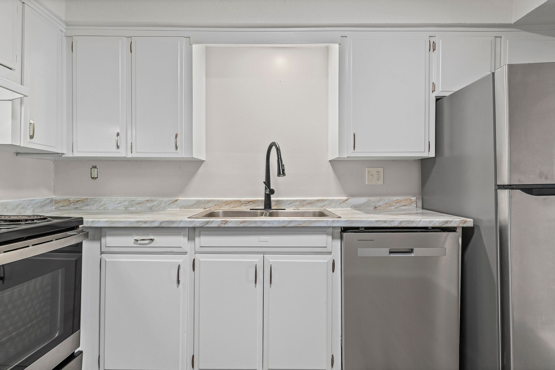 White kitchen with stainless steel appliances and a black faucet.