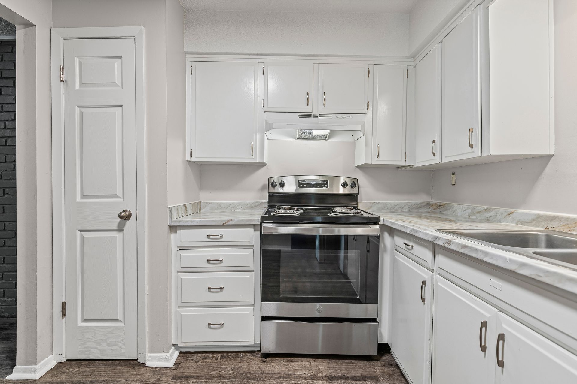 White kitchen with stainless steel stove, white cabinets, and gray countertops.