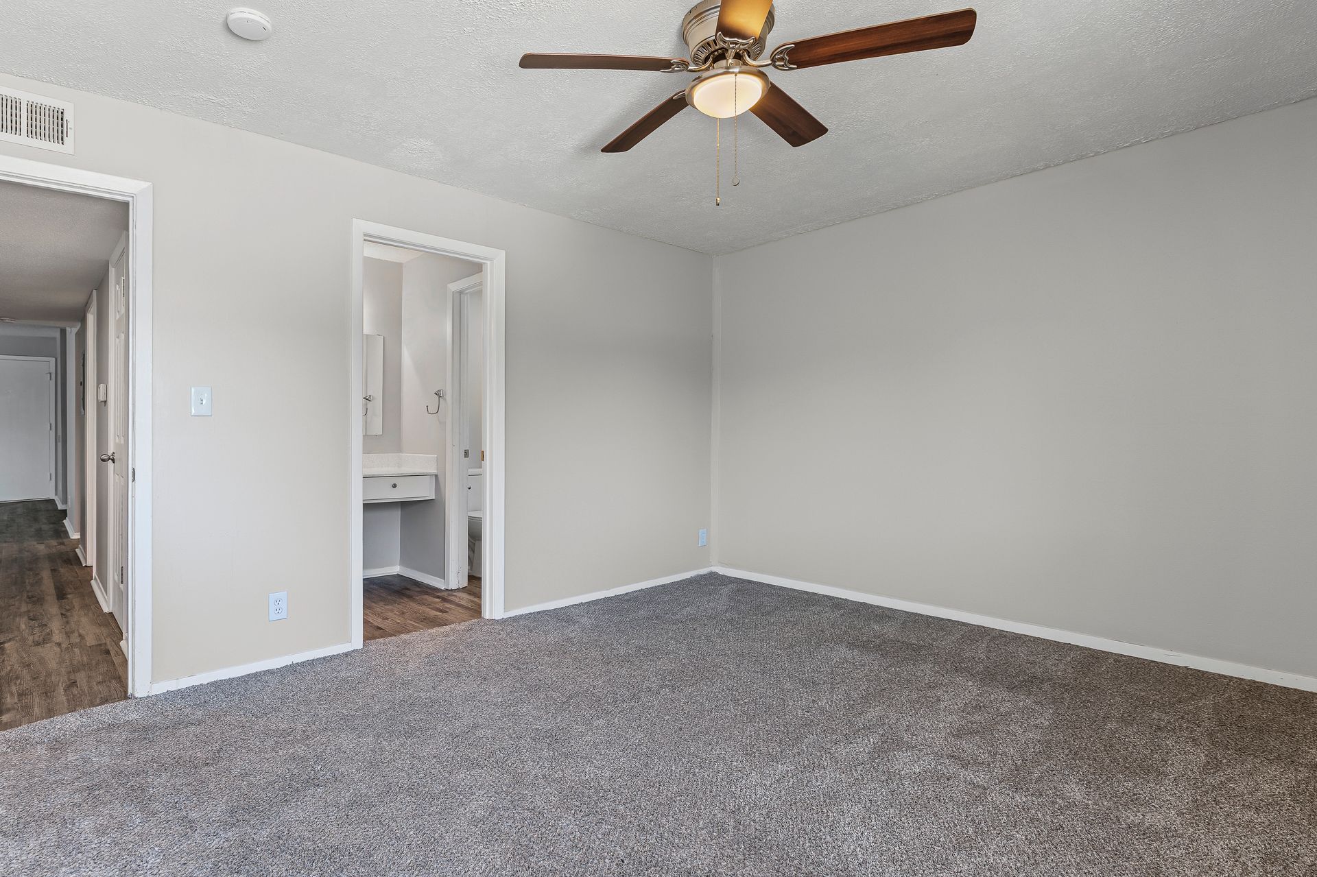 Empty bedroom with gray carpet, light gray walls, and open doorways.