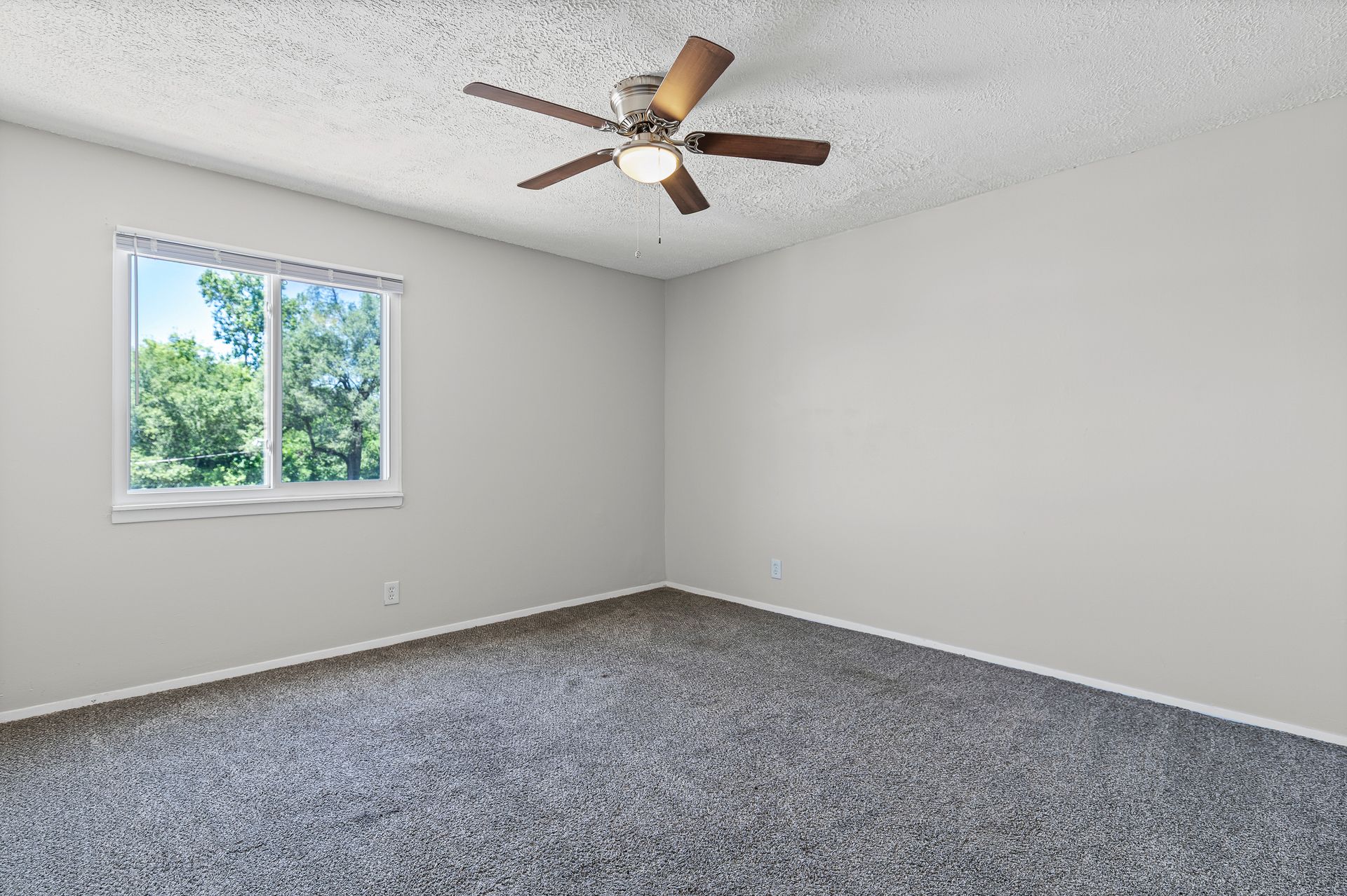 Empty bedroom with gray carpet, white walls, a window, and a ceiling fan.