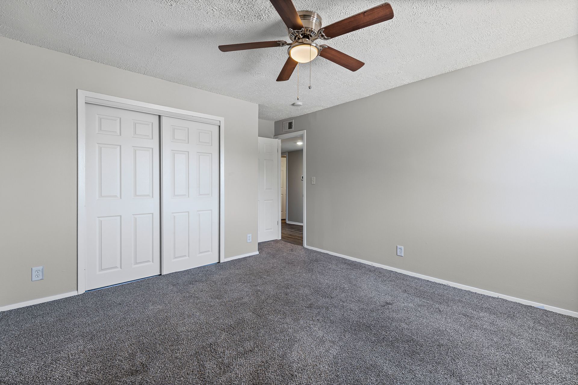 Empty bedroom with gray carpet, white closet doors, and a ceiling fan.