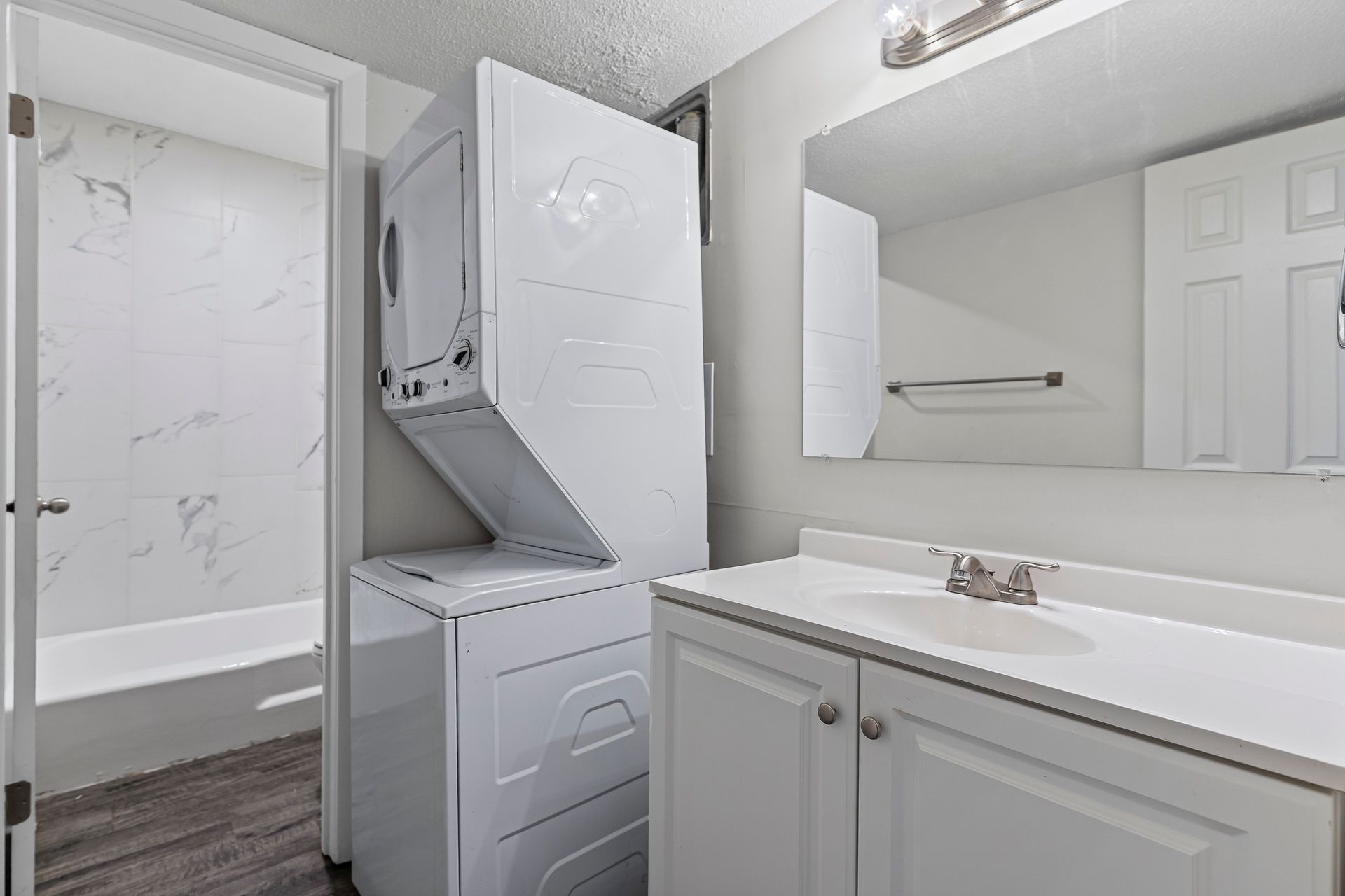 Bathroom with white vanity, stacked washer/dryer, and shower/tub visible through doorway.