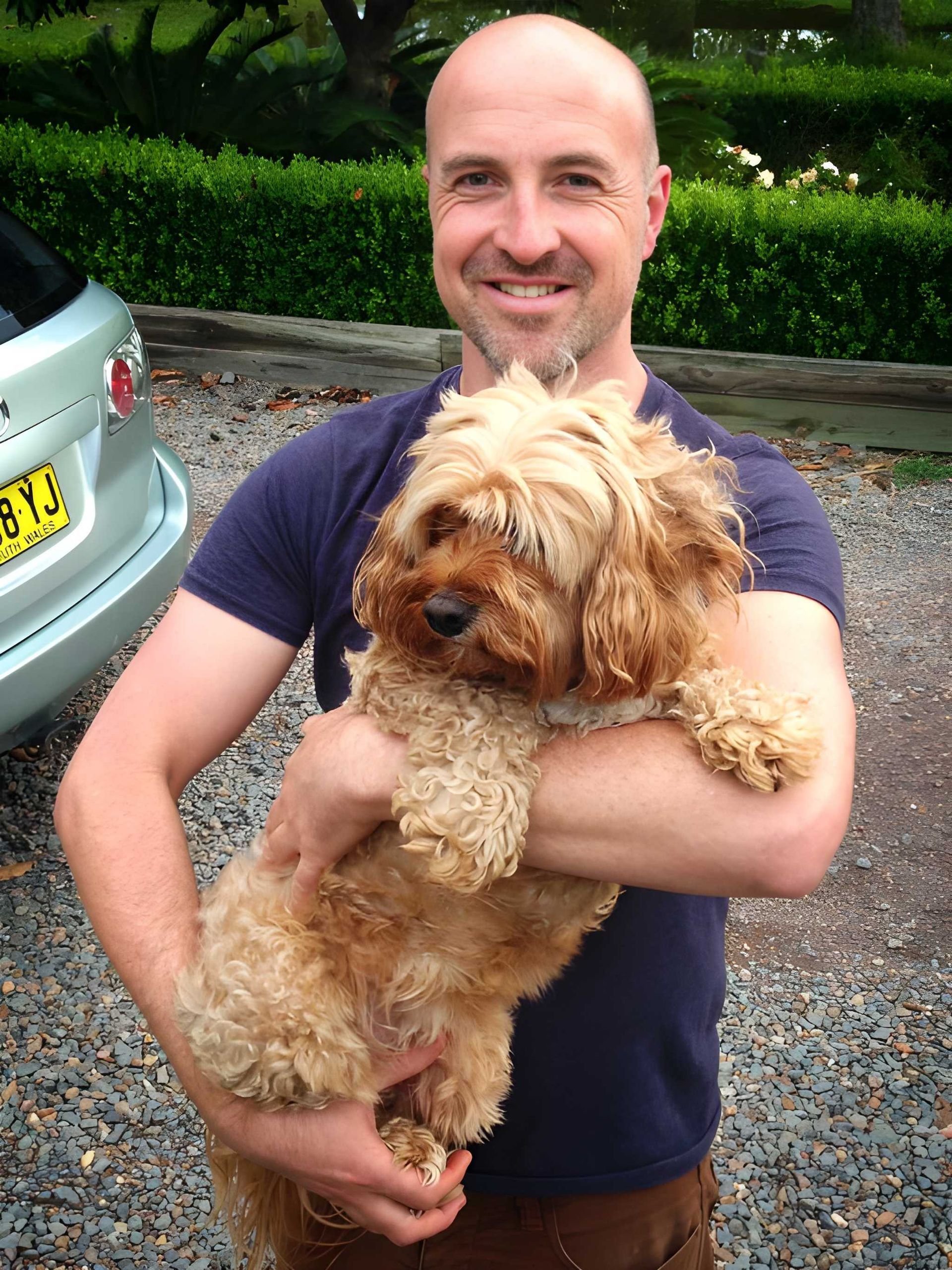 Man Holding a Small, Brown, Curly-haired Dog Outside — Auramist Lodge Dog Boarding & Cattery In Salt Ash, NSW
