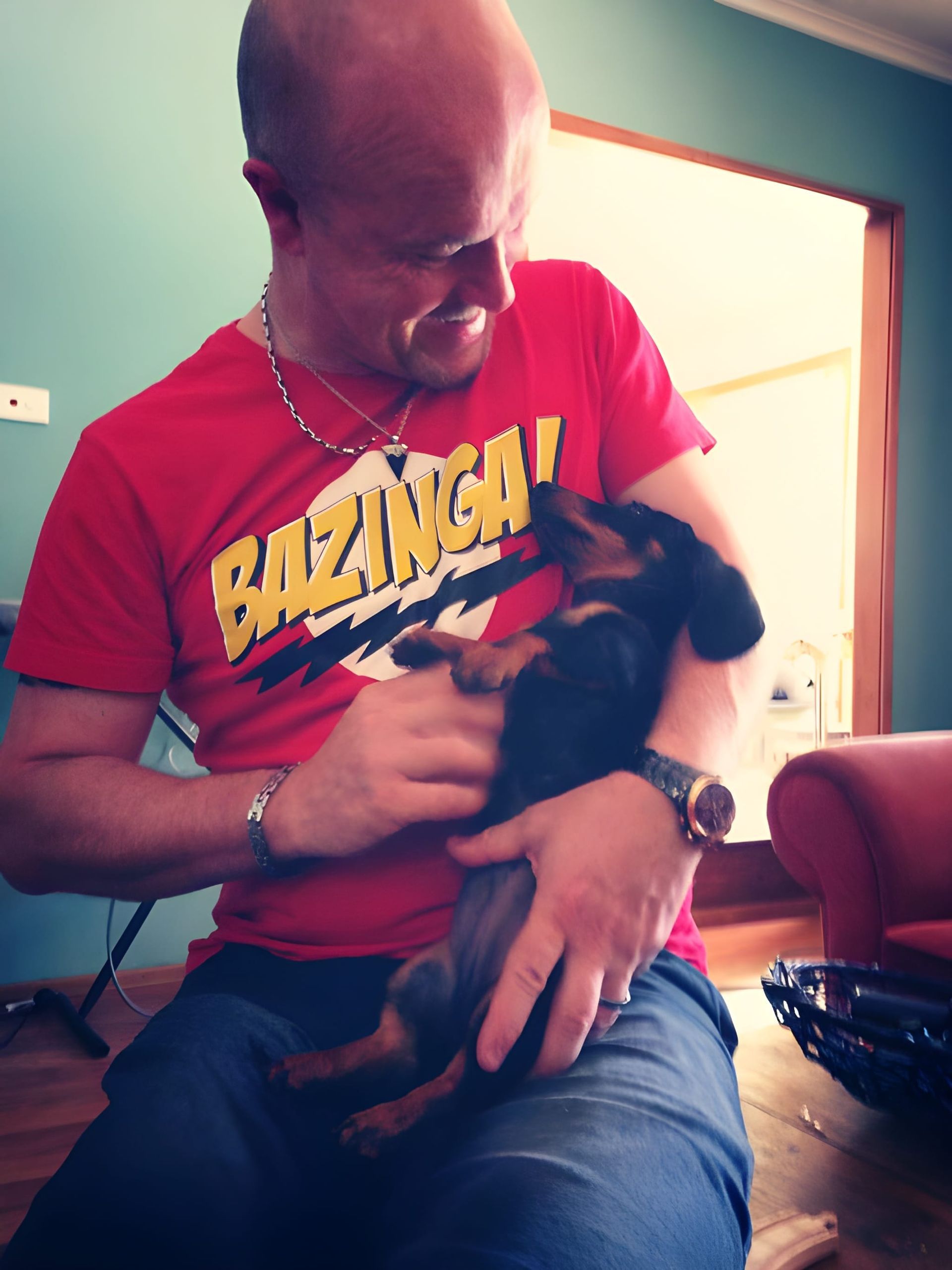 Man in Red Shirt Holding a Small Black Dog Indoors — Auramist Lodge Dog Boarding & Cattery In Salt Ash, NSW