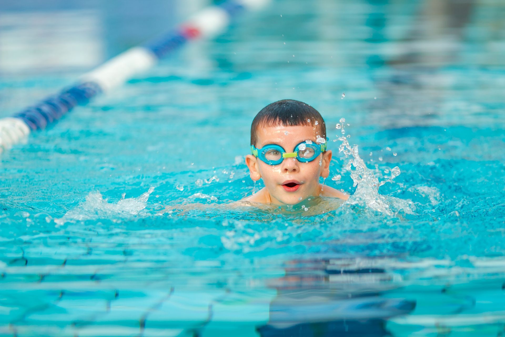 A young boy wearing goggles is swimming in a swimming pool.