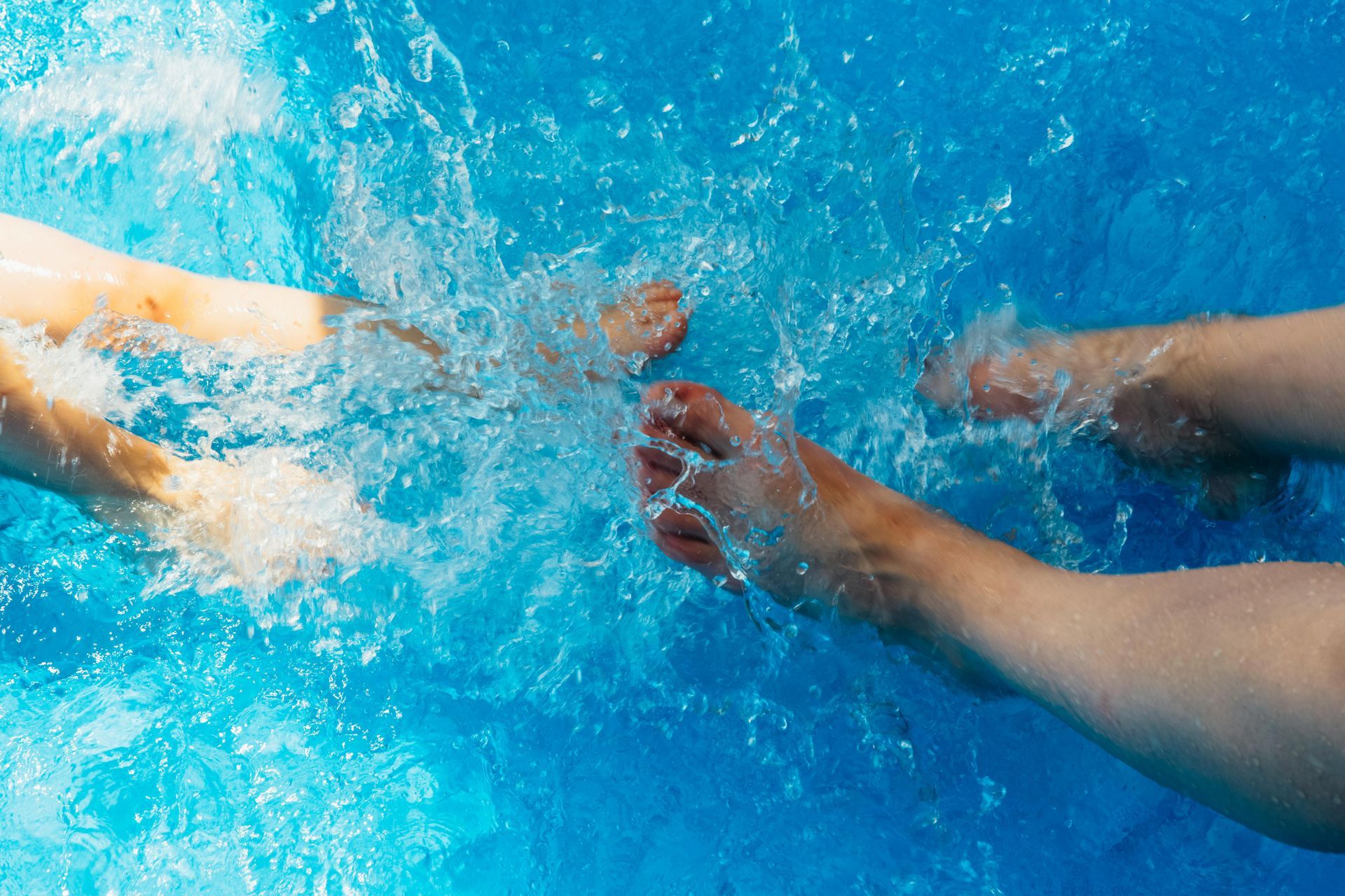 Two people 's feet are splashing in a swimming pool.