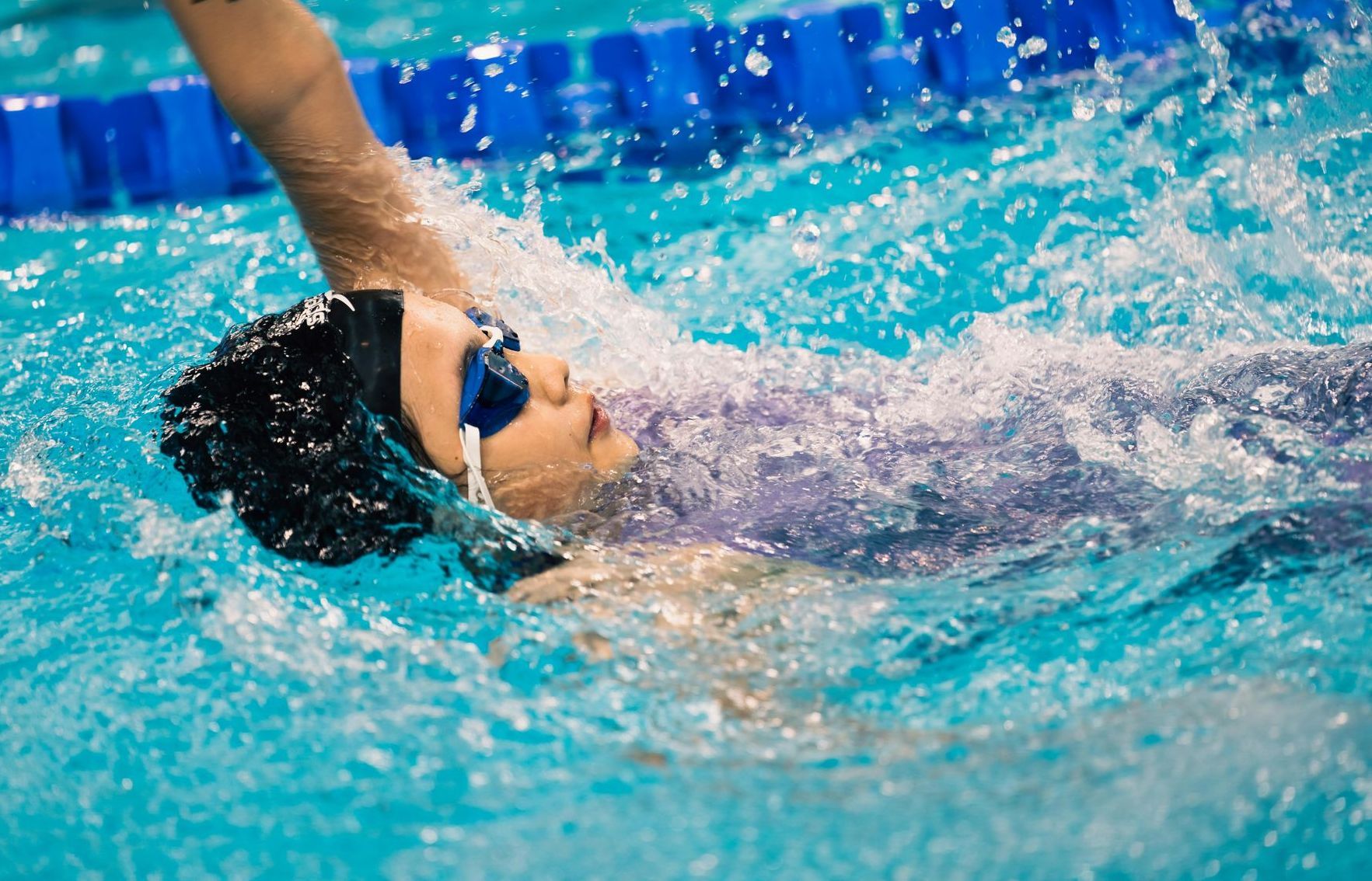 A woman is swimming in a swimming pool wearing goggles.