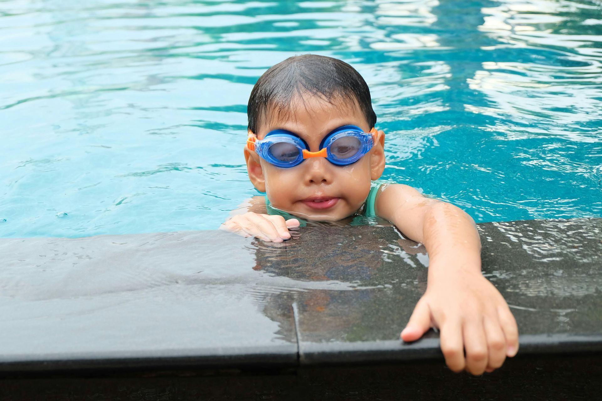 A young boy wearing goggles is swimming in a pool.