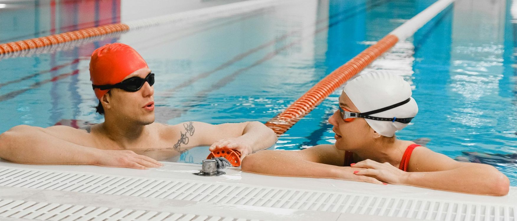 A man and a woman are sitting on the edge of a swimming pool.