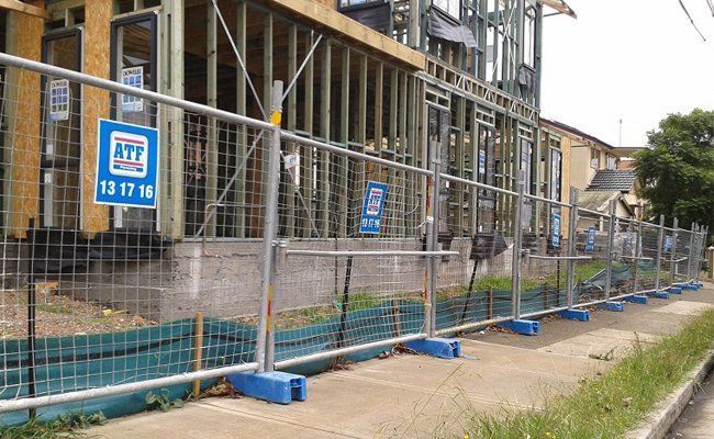 A fence is surrounding a building under construction on the side of the road.
