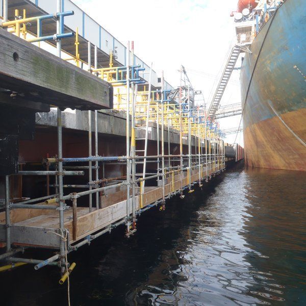 A large ship is docked next to a dock with scaffolding